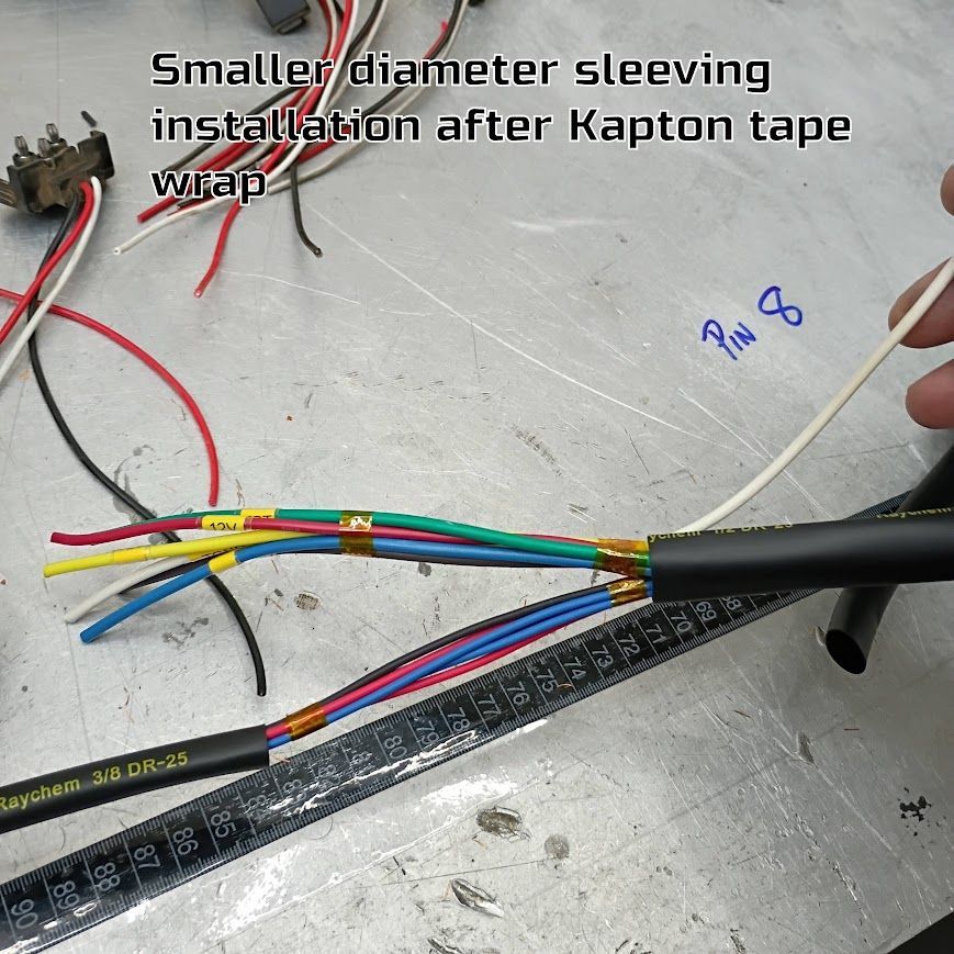 Multicolored wires being sleeved on a workbench, with handwritten note “Smaller diameter sleeving installation after Kapton tape wrap.”