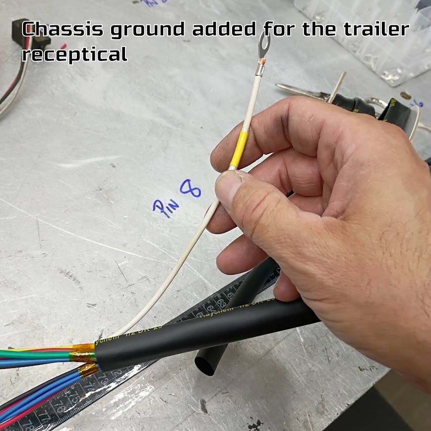 Hand holding a yellow wire near a cable bundle on a workbench, with text noting chassis ground for trailer receptacle