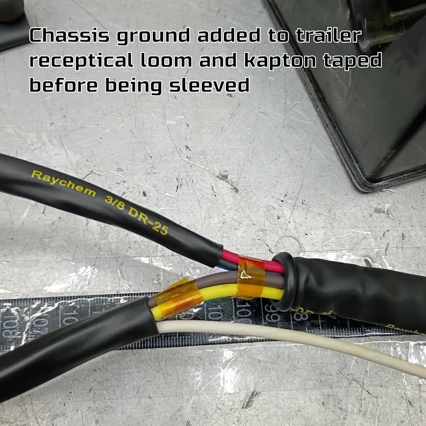 Black and red wires in a loomed cable harness, taped and sleeved on a metal workbench.