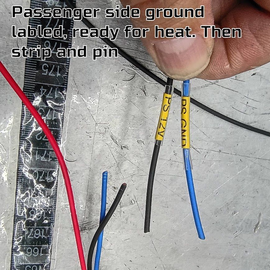 Hand holding black, blue, and red wires with labels over a scratched metal surface.