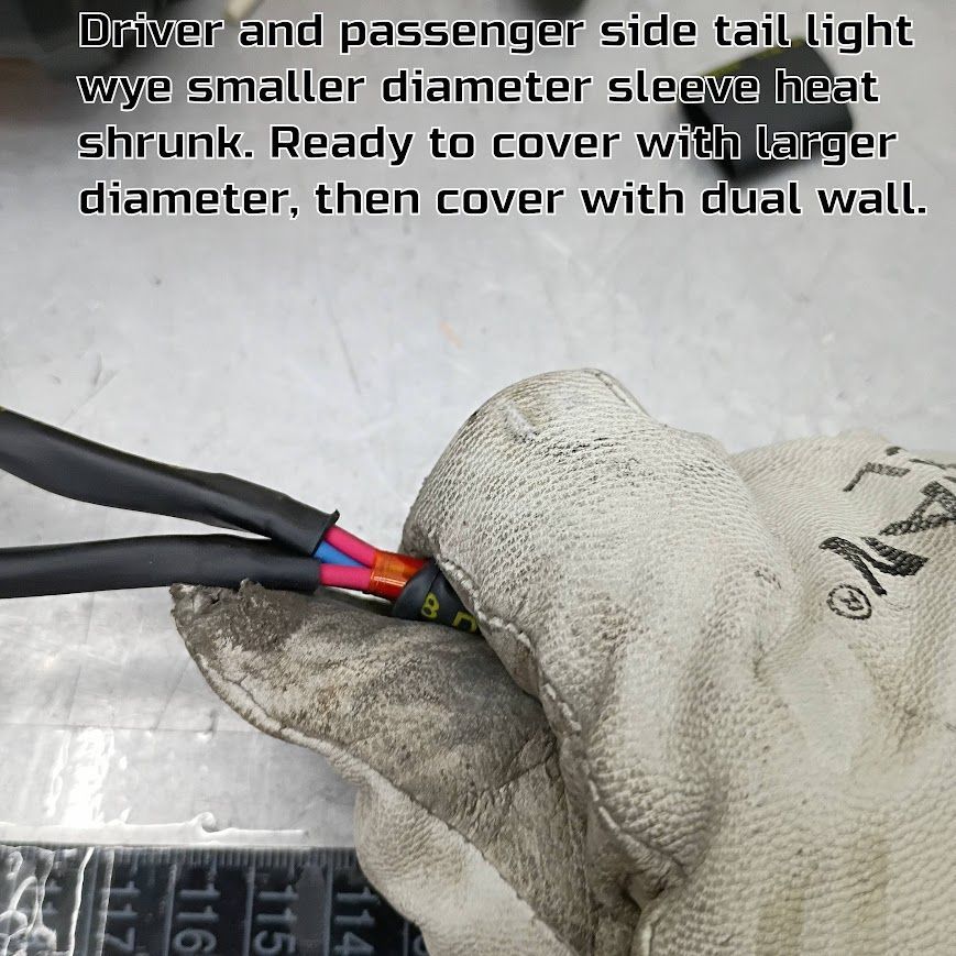 Gloved hands shrink-wrap exposed wire connectors on a cable harness with black, red, and blue wires.