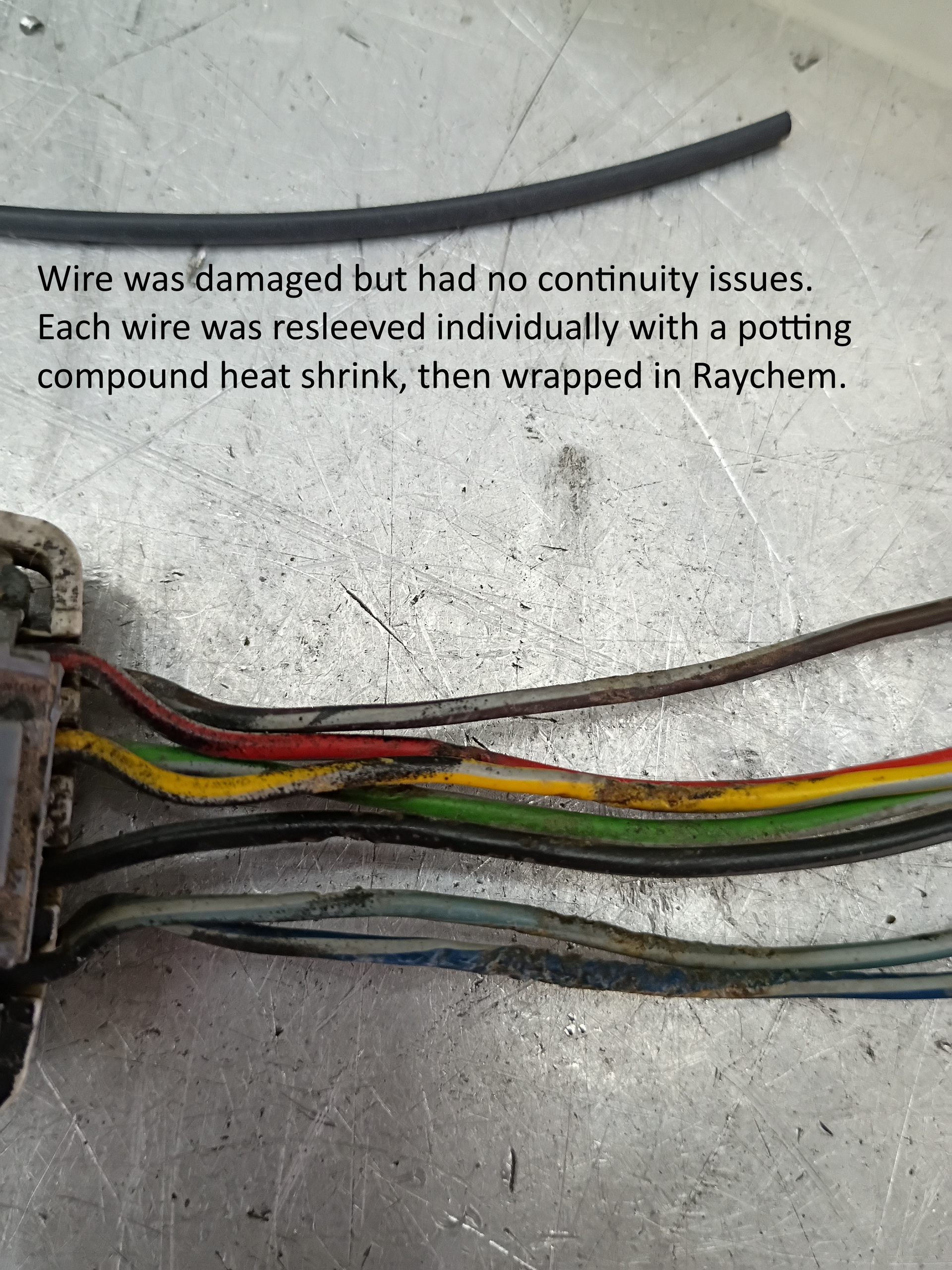 Damaged multicolor wire bundle with heat-shrink tubing on a work surface, showing repaired connections