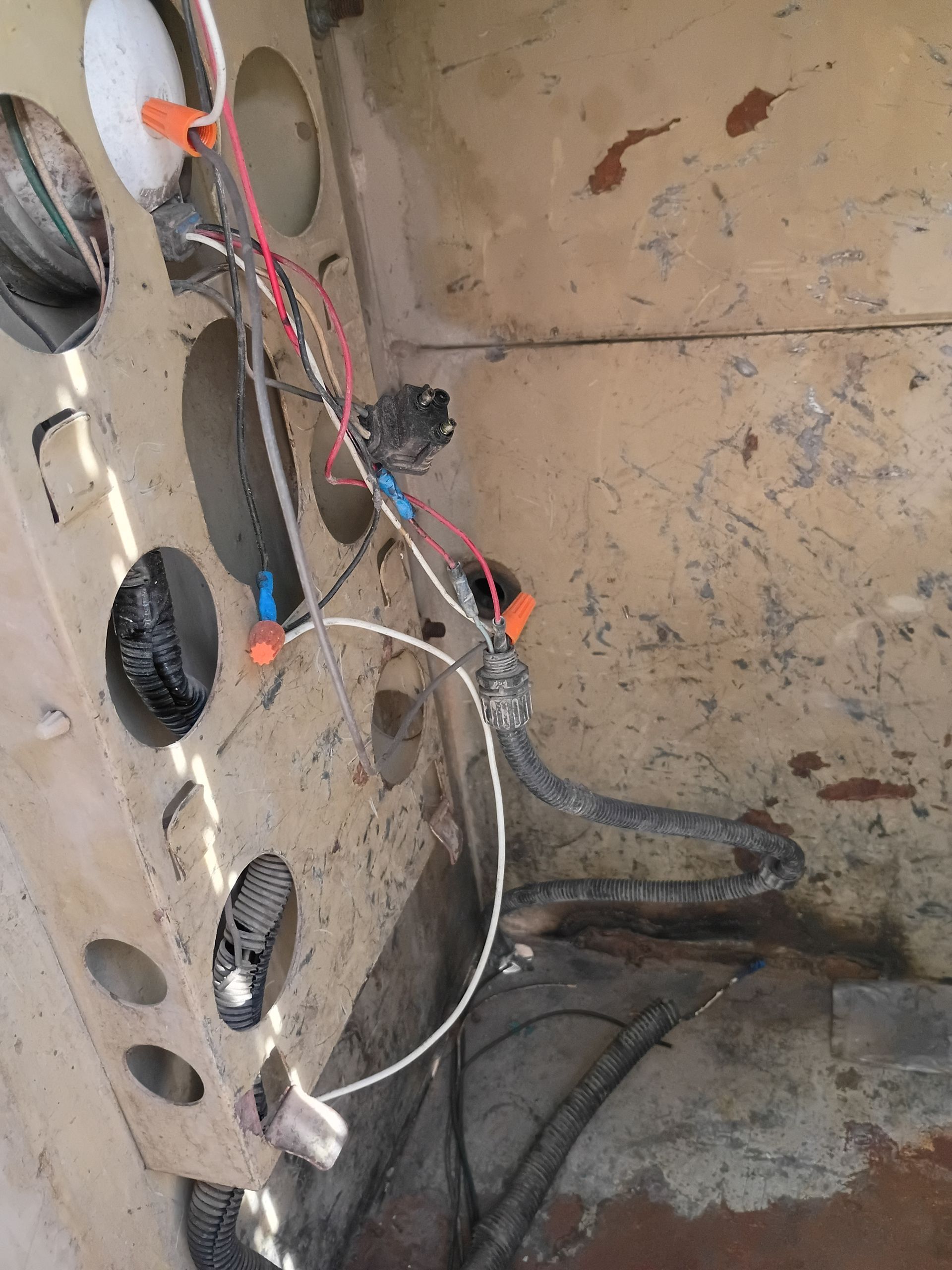 Worn cardboard with tangled wires, orange clips, and black oval pieces on a dirty floor.