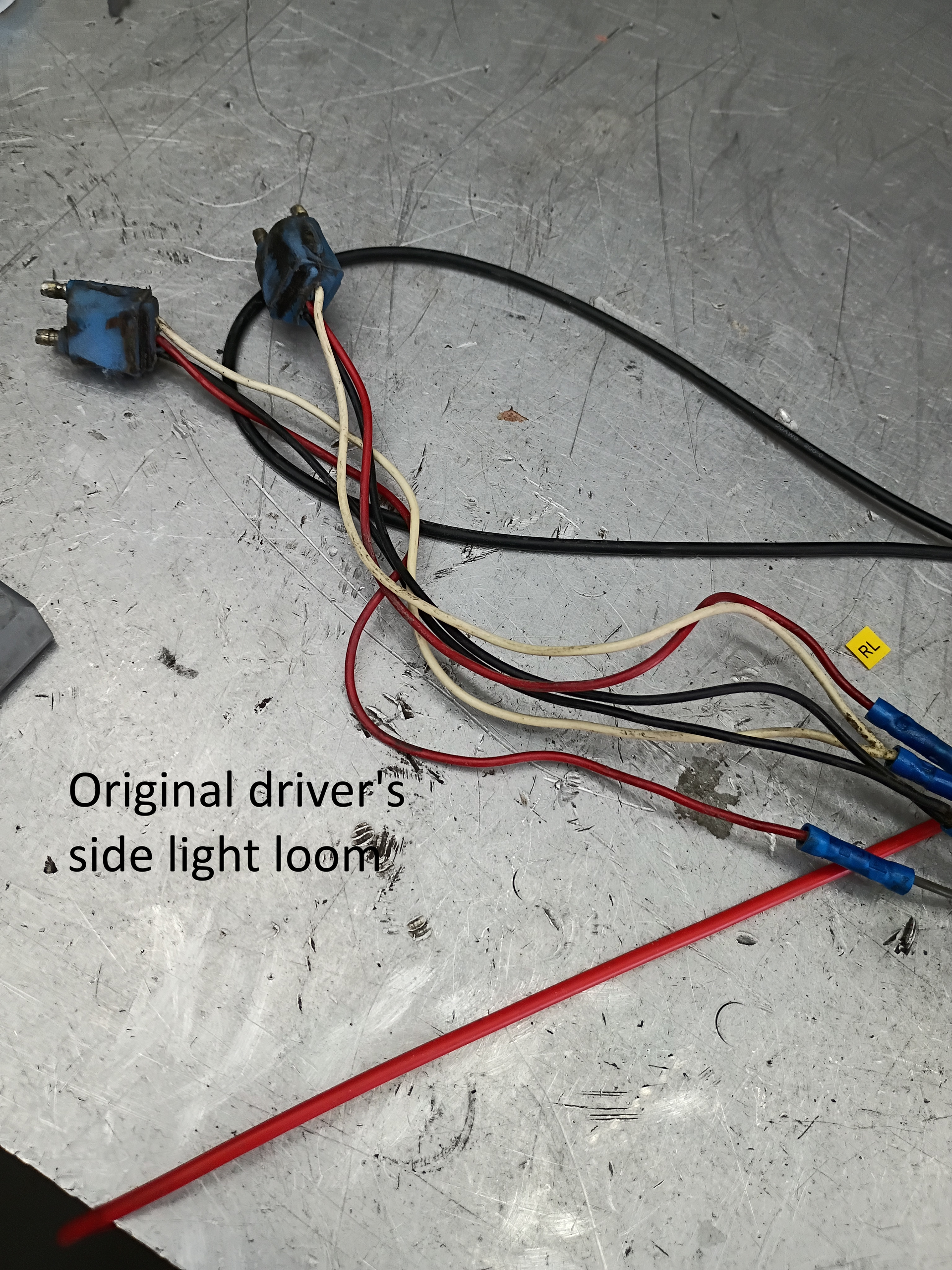 Car wiring harness with connectors and red, black, and yellow wires on a concrete floor.
