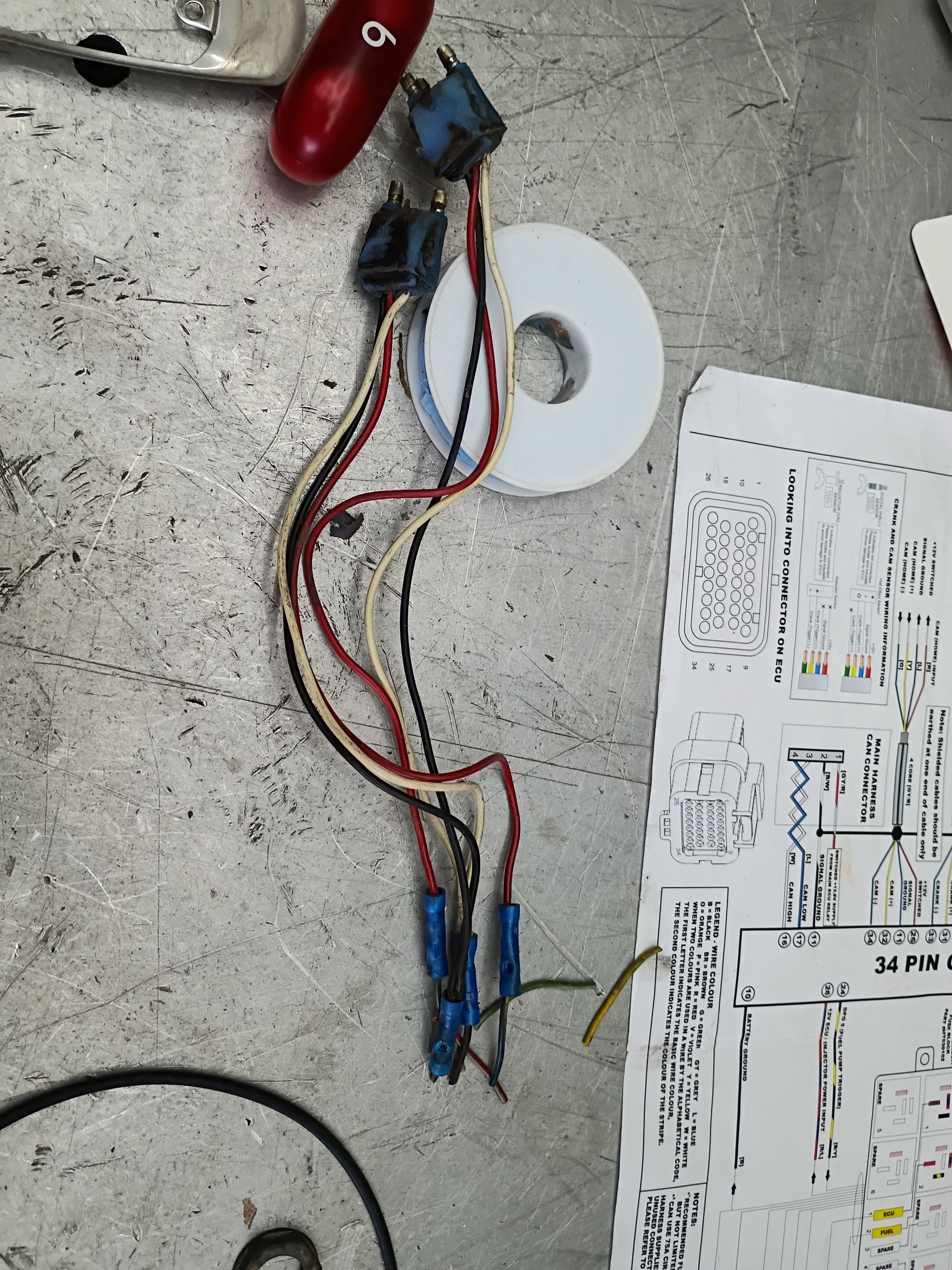 Wires and connectors on a concrete floor beside a printed diagram and red-handled tool.