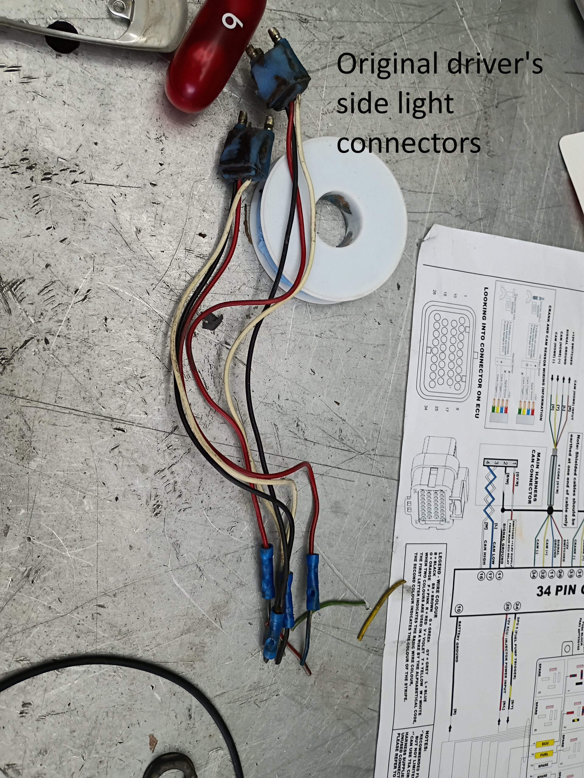 Car side light wiring connectors on concrete, with a wiring diagram partially visible nearby