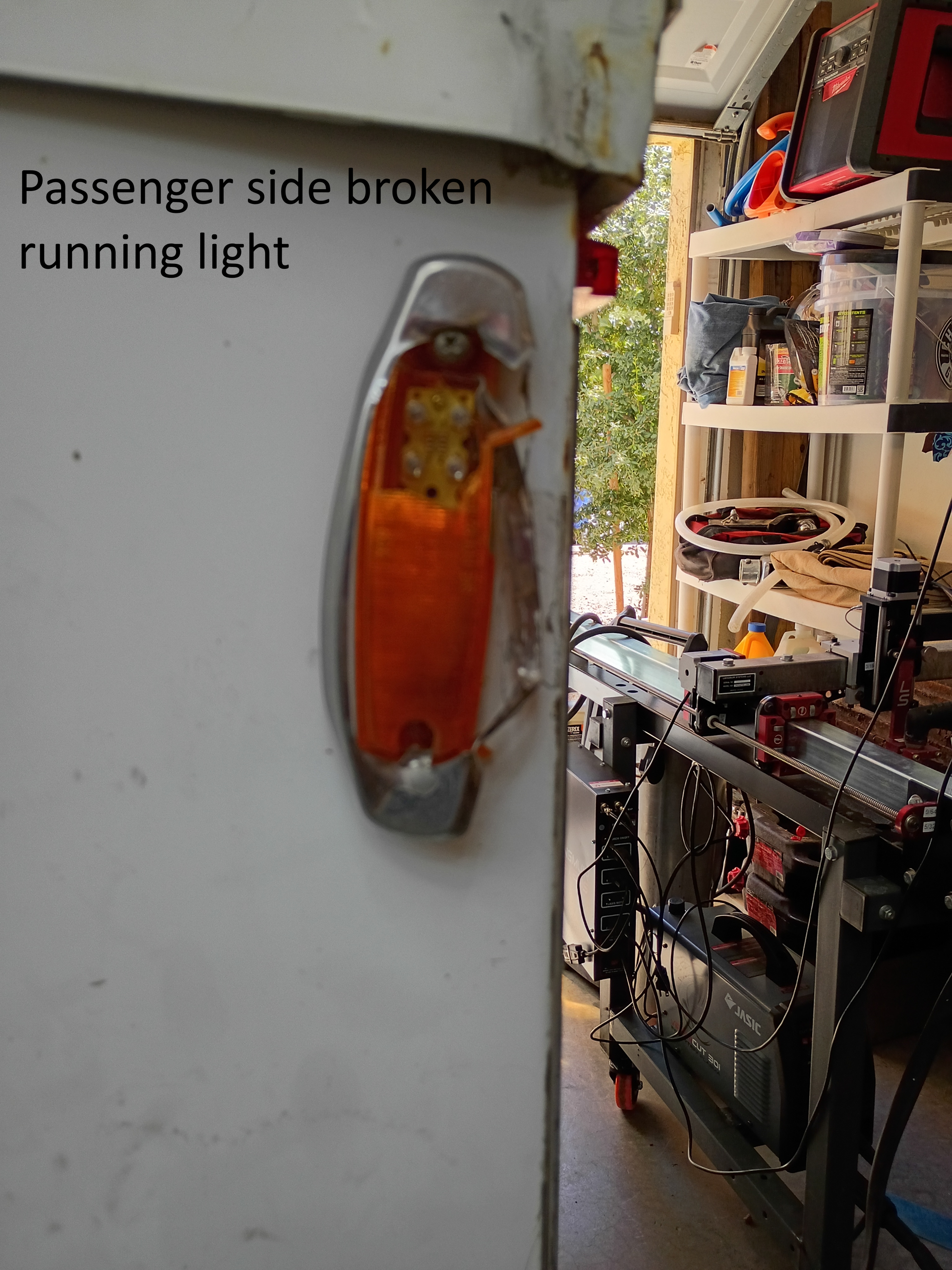 Close-up of a broken amber passenger-side running light on a white vehicle, with garage shelves in the background
