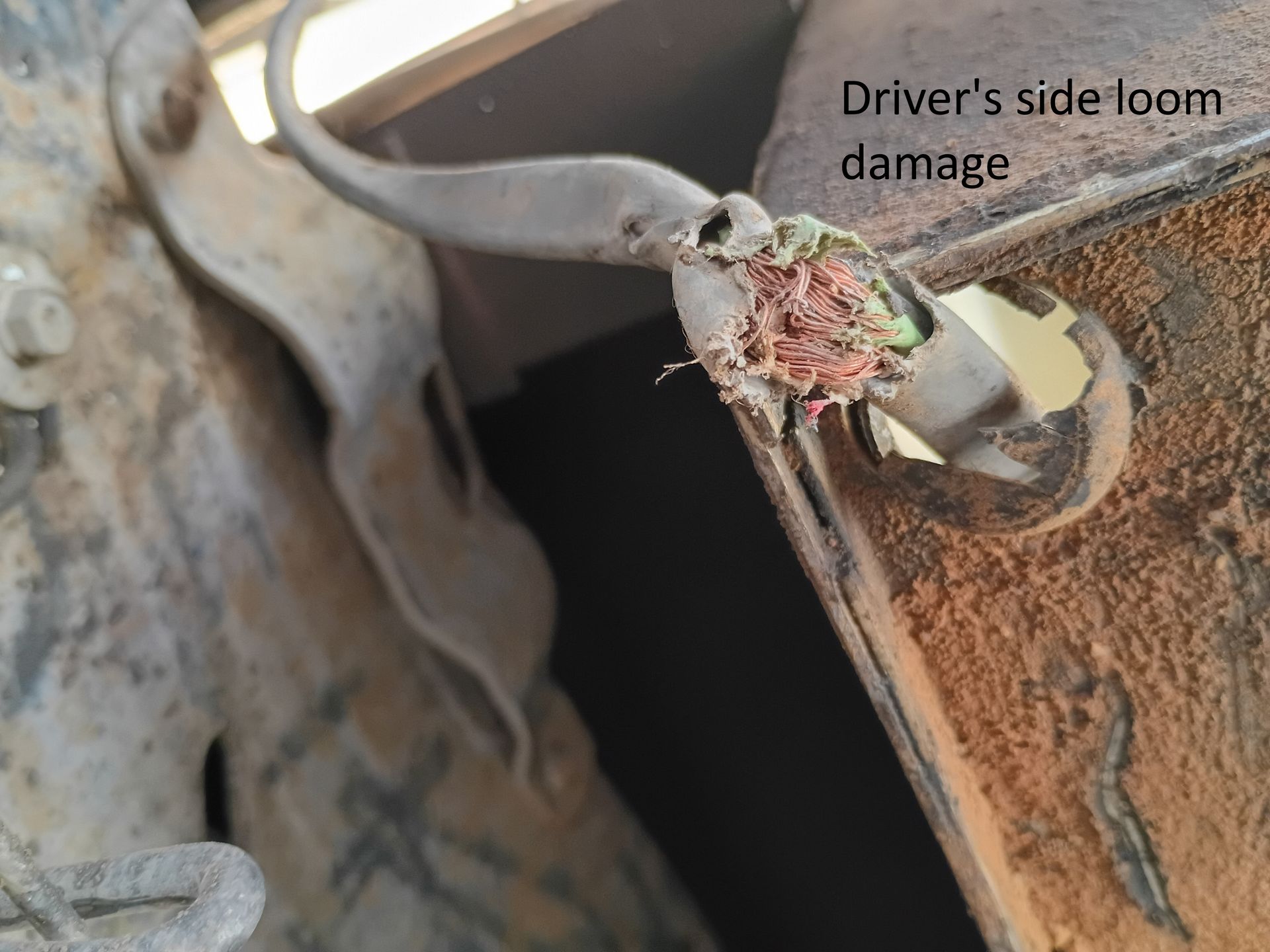 Close-up of rusted vehicle metal with torn driver’s side door frame damage near the hinge.