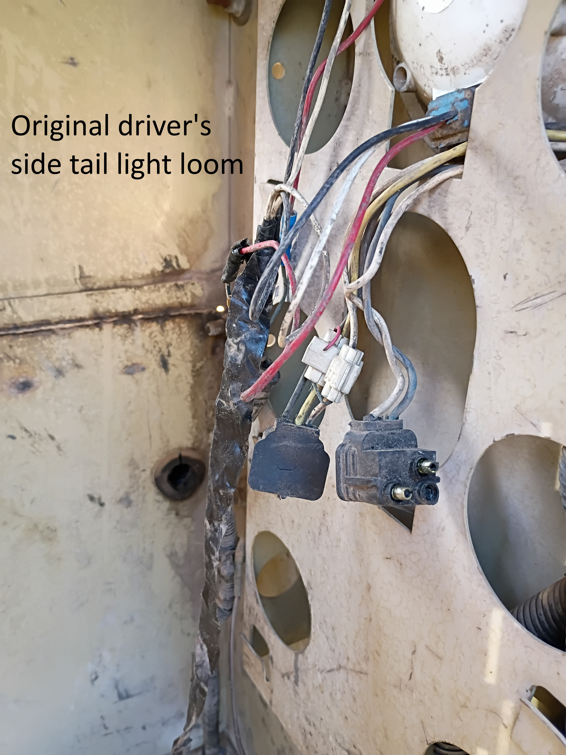 Damaged driver-side tail light wiring harness hanging from a beige vehicle panel with circular cutouts