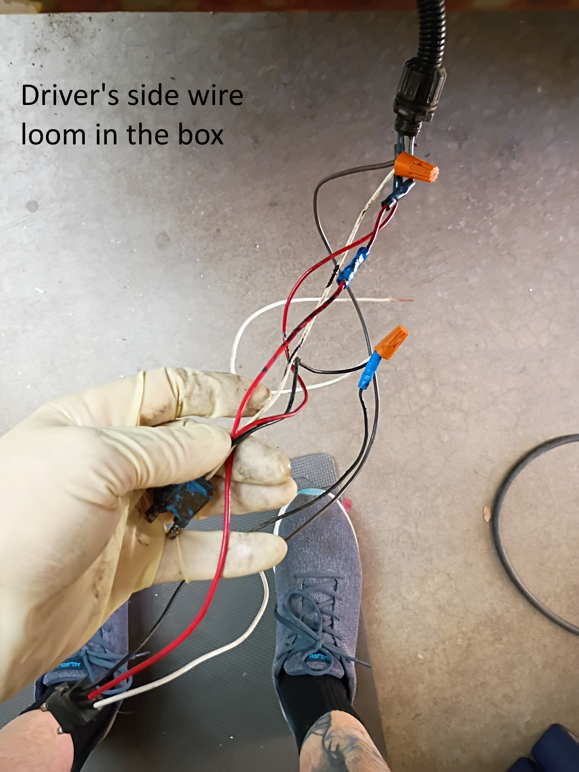 Driver’s side wire loom in a box, with bundled red, white, and black wires being held by gloved hands.
