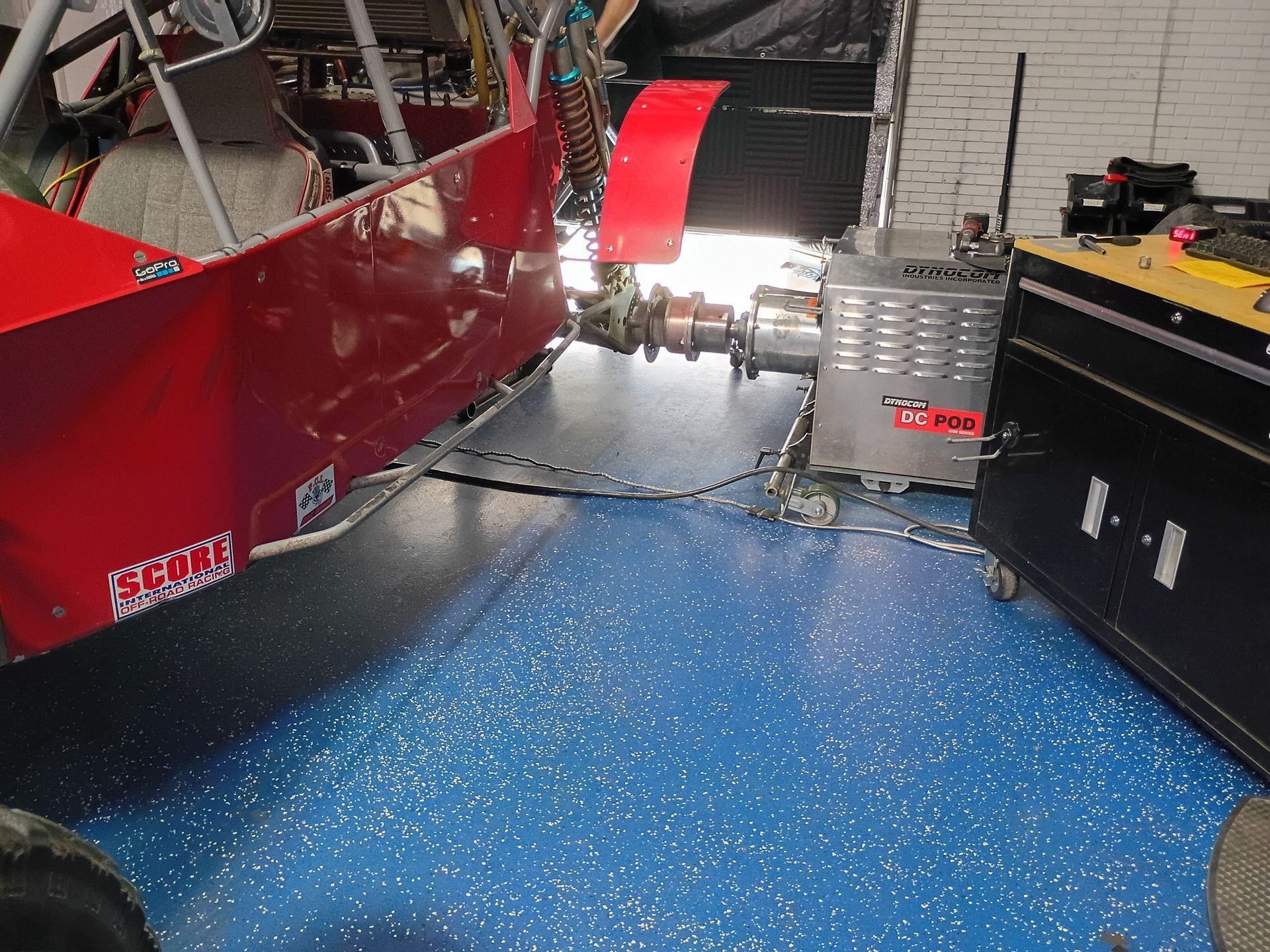 Red racing car connected to a dyno in a garage with blue speckled floor.