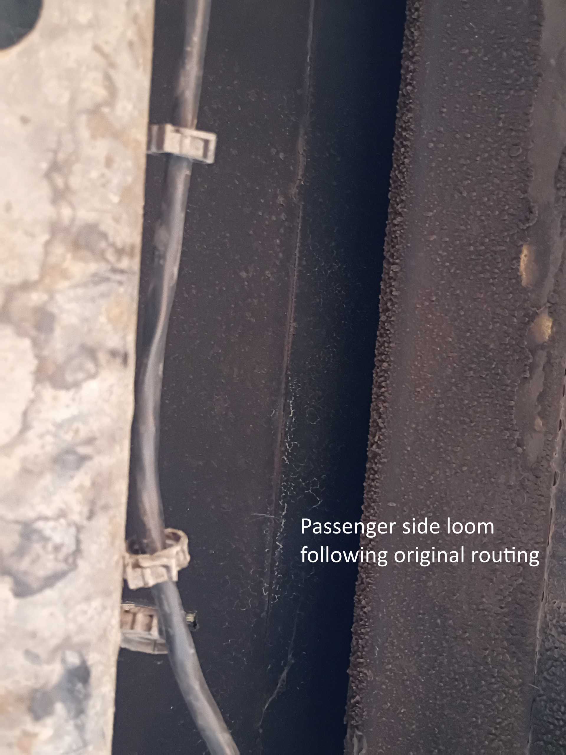 Passenger side floor by a panel gap, with text noting original routing of a wire or hose