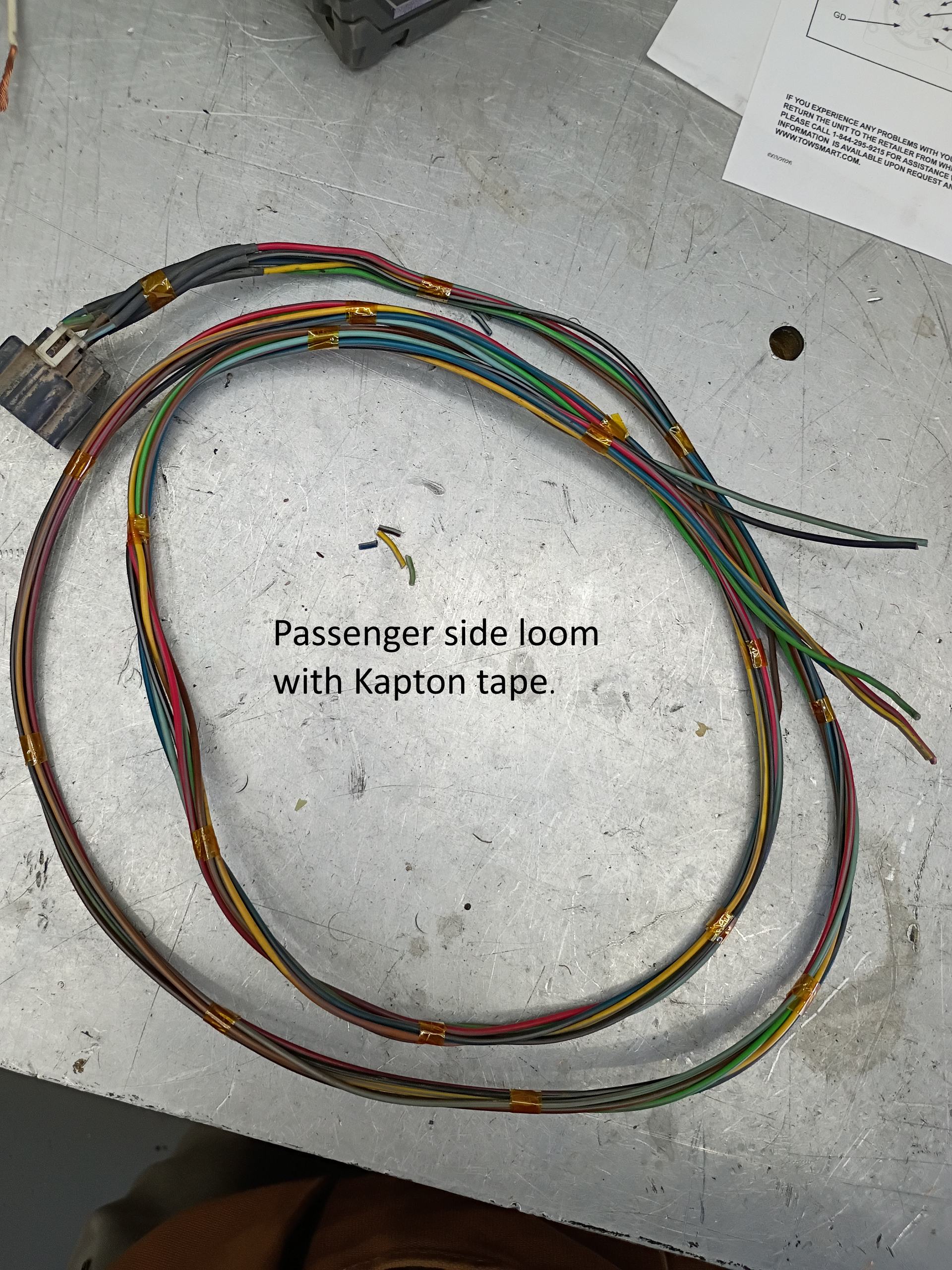 Coiled multicolored wire harness on a gray floor, labeled with text about a passenger-side loom and Kraton tape.