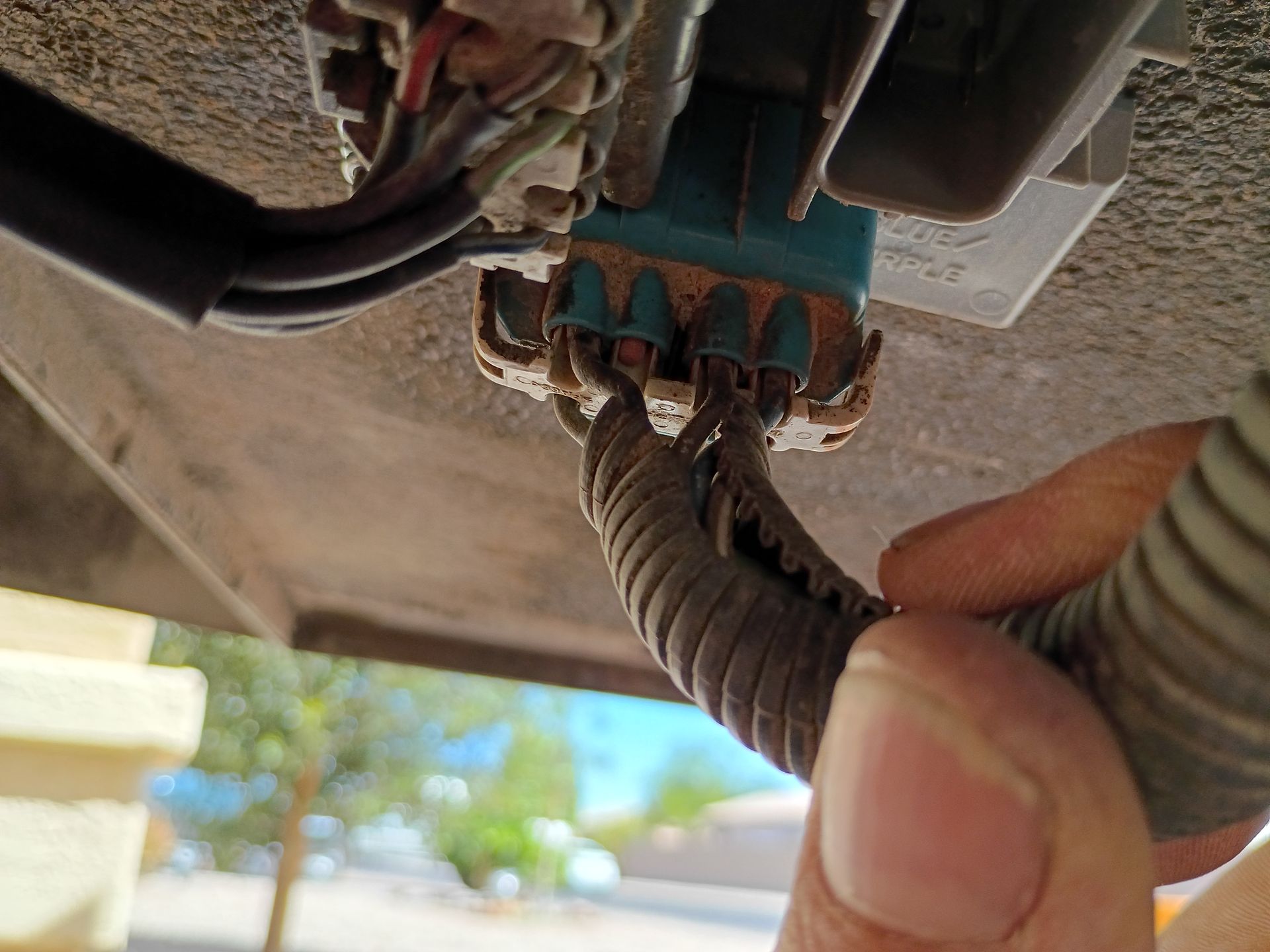 Hands connecting wires to a blue electrical connector under a vehicle.