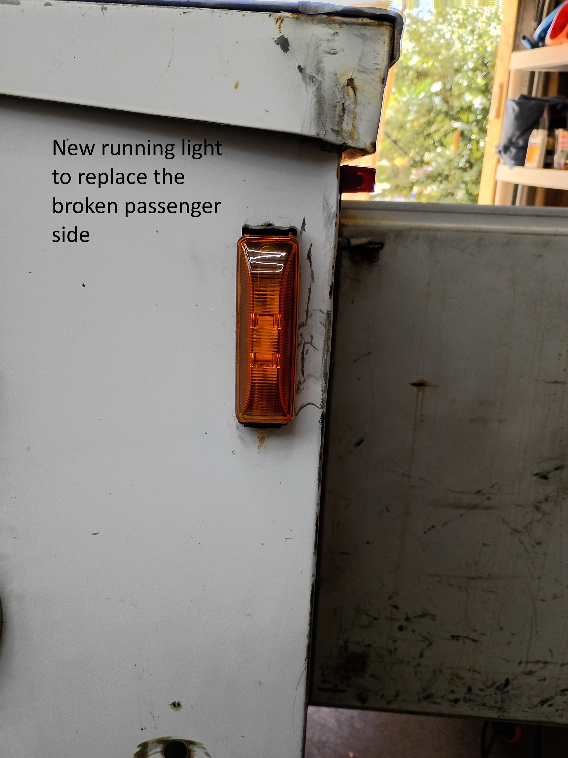 White vehicle side with amber marker light and handwritten note about a broken passenger-side running light