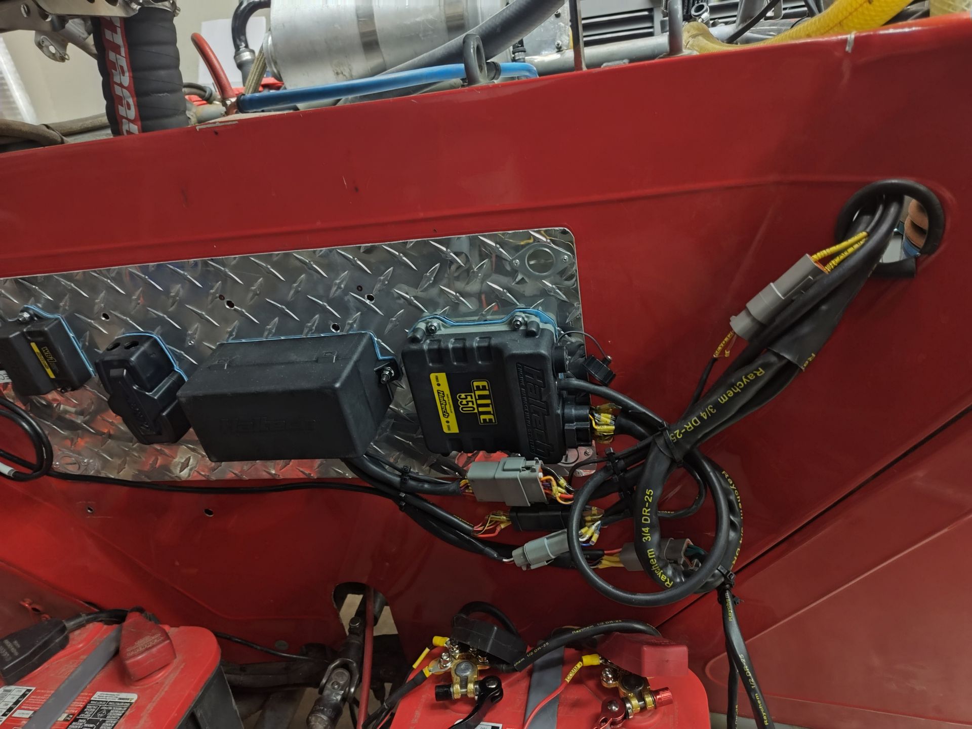 Red metal panel with wiring, control boxes, and a diamond-plate section in an industrial setting