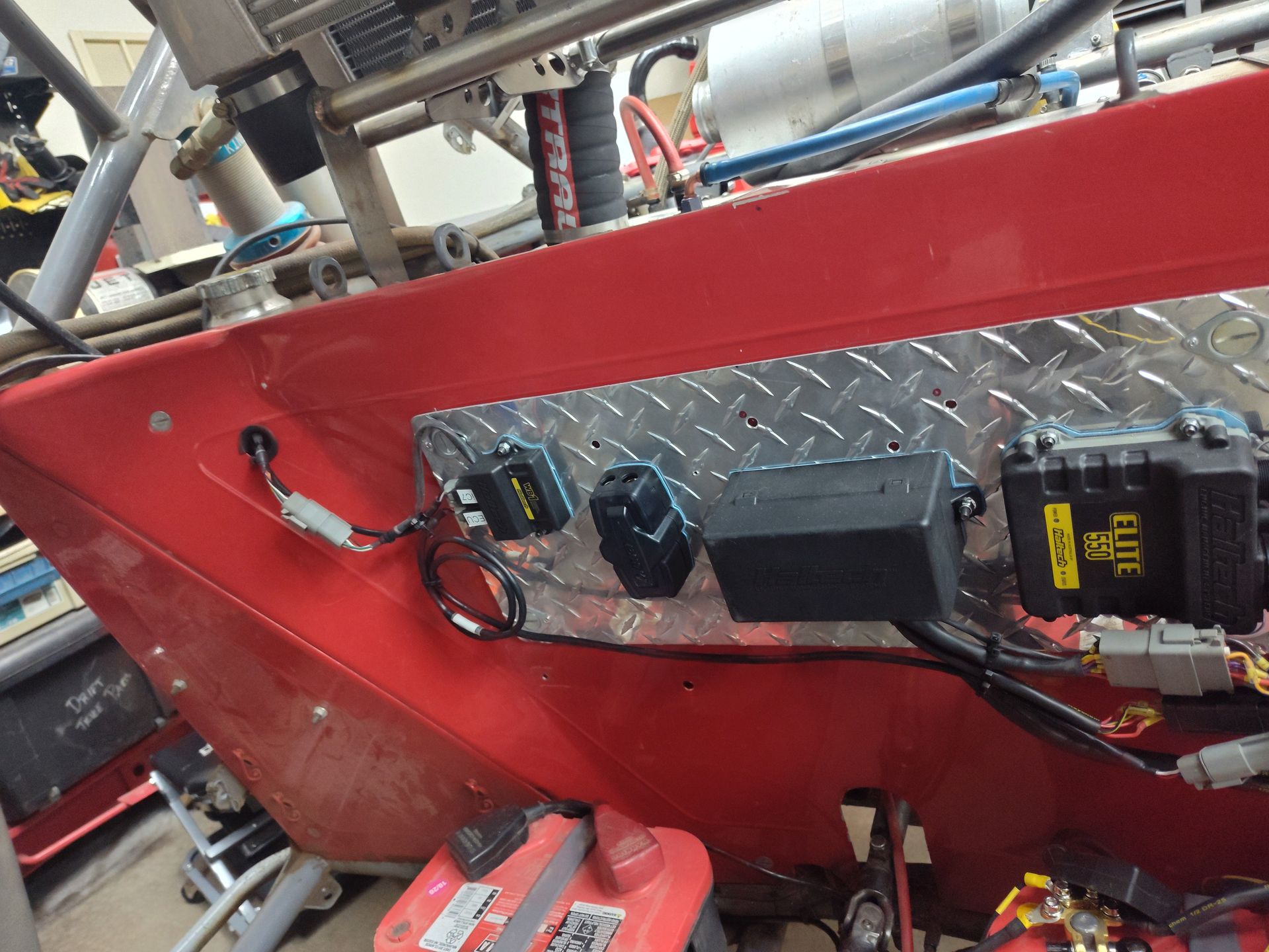 Red metal machine panel with switches, wiring, and control boxes mounted on diamond plate.