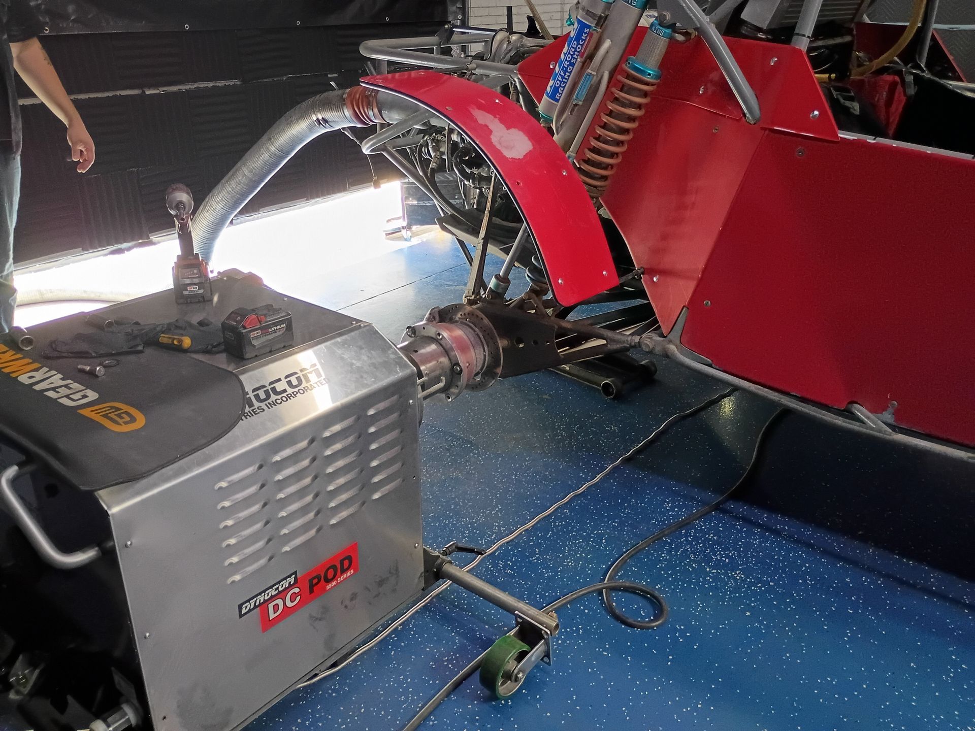 Industrial machine with red metal parts and a gray power unit on a blue floor, with hoses attached
