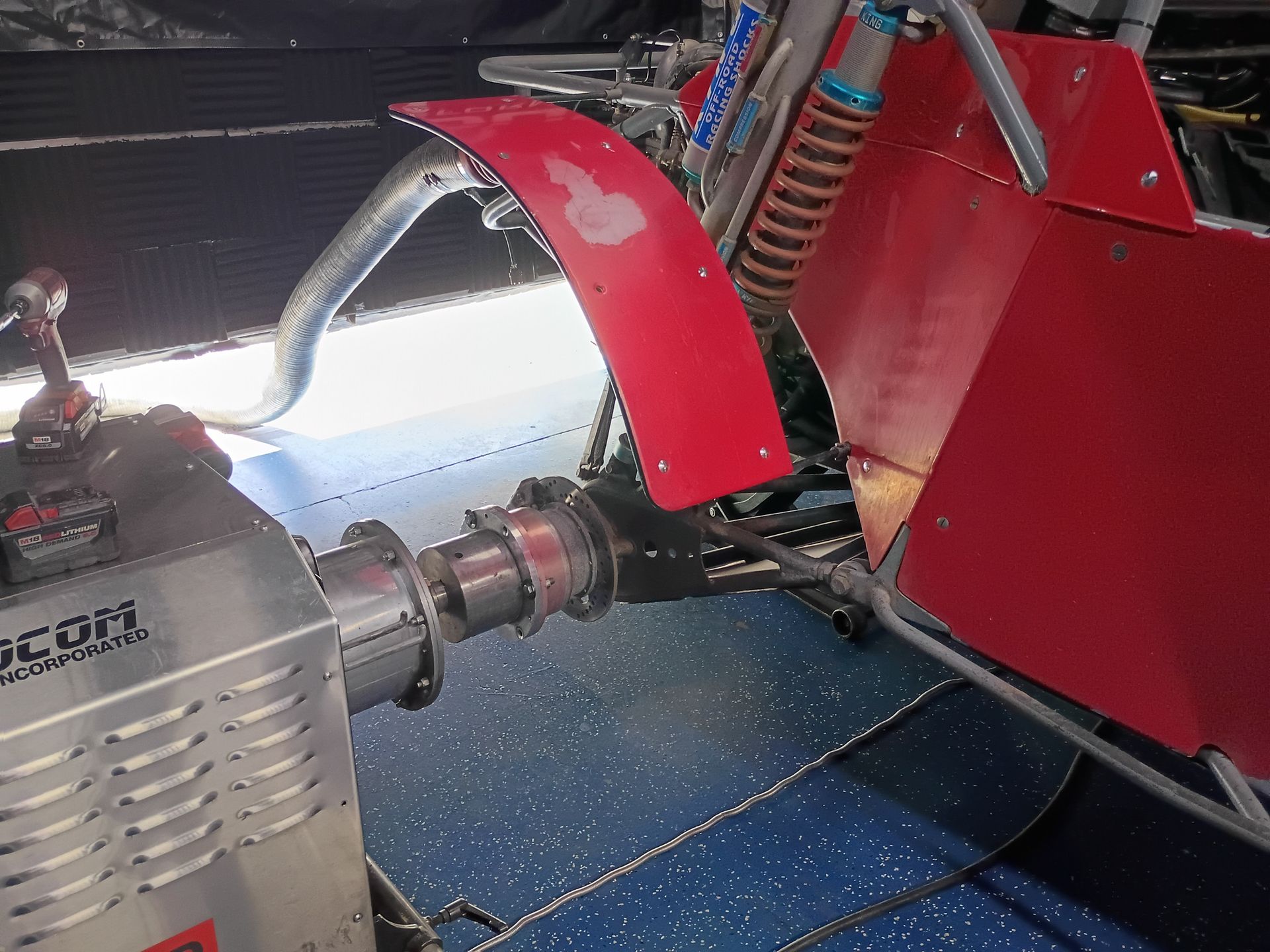 Red race car engine and suspension close-up with silver engine block and red body panels