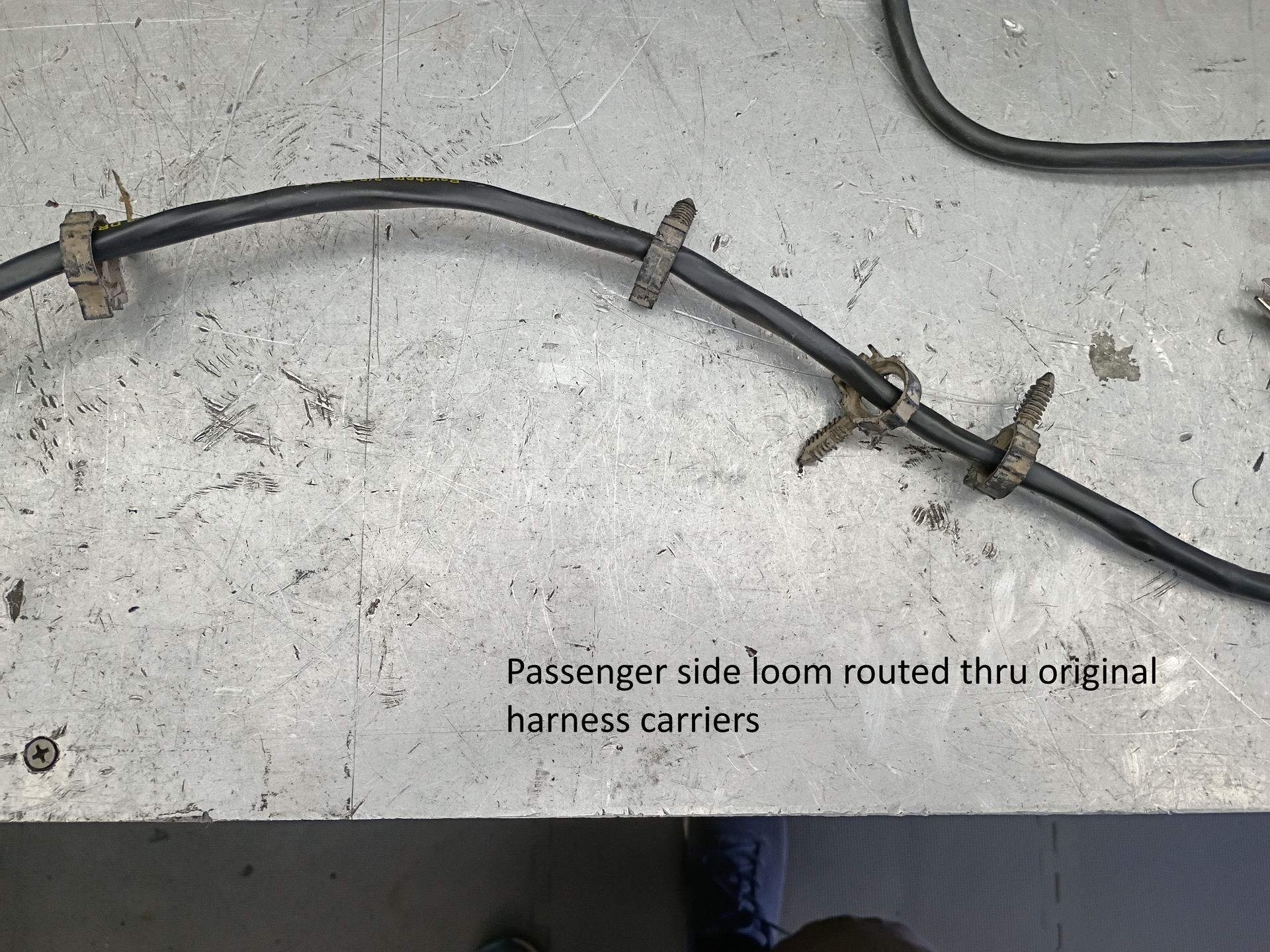 Black passenger-side wiring loom on concrete, routed through original harness carriers, with damage visible