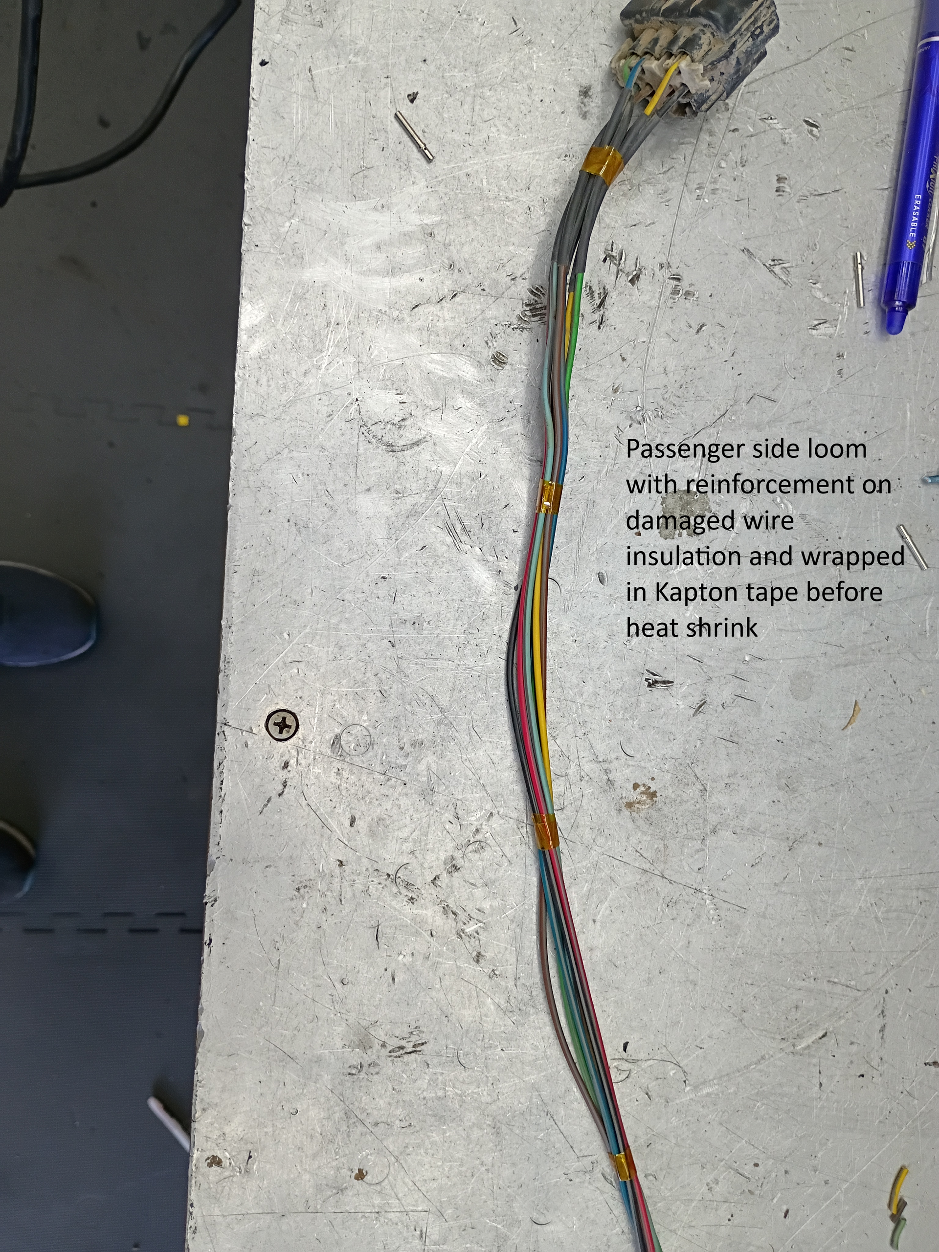 Loose multicolored wiring harness on a light tabletop beside a blue pen and printed text.