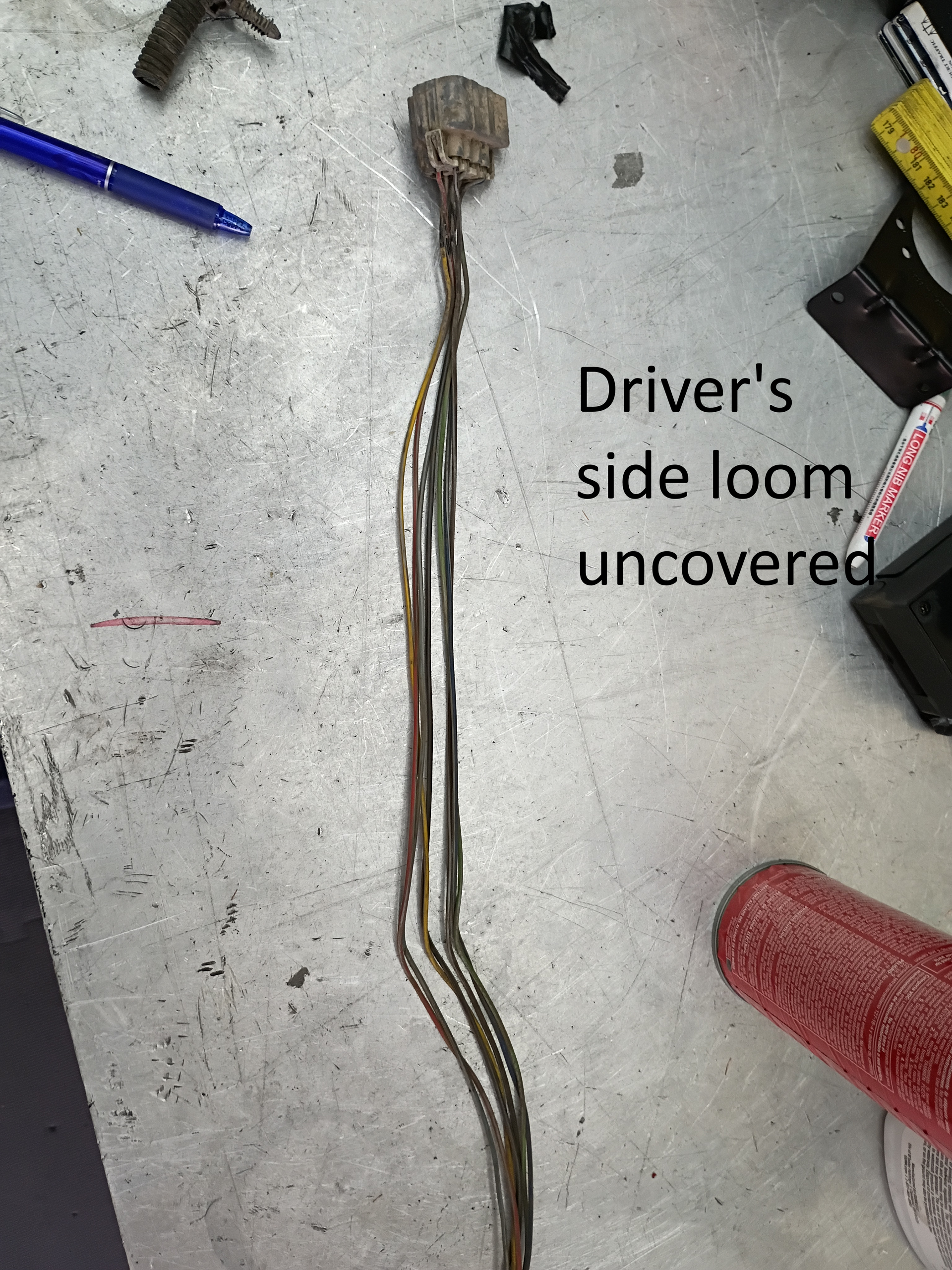 Damaged driver’s side wiring loom on a concrete floor, with the outer cover removed.