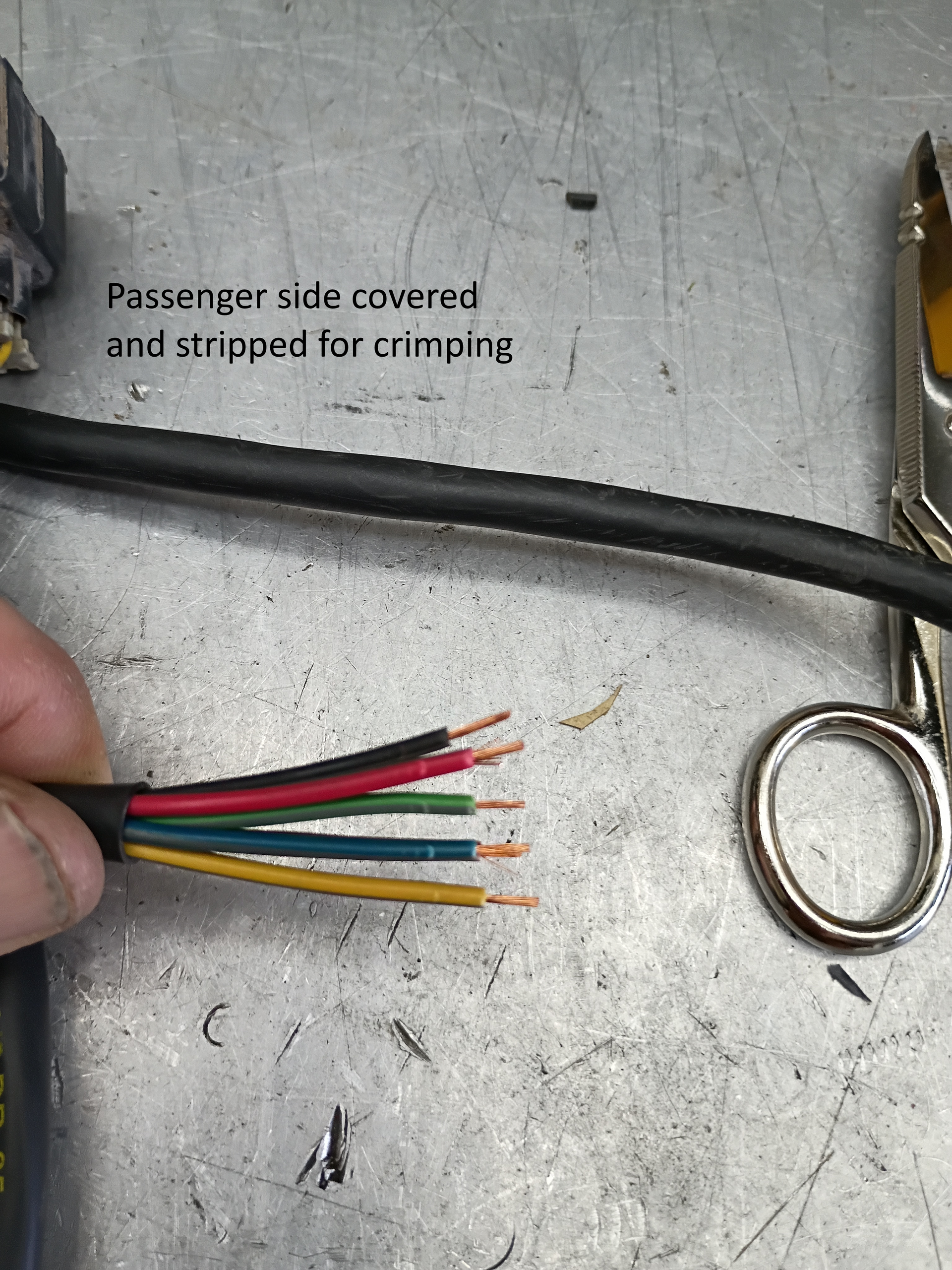 Hand holding a stripped multi-colored wire next to a cable marked for crimping, with a ring terminal nearby