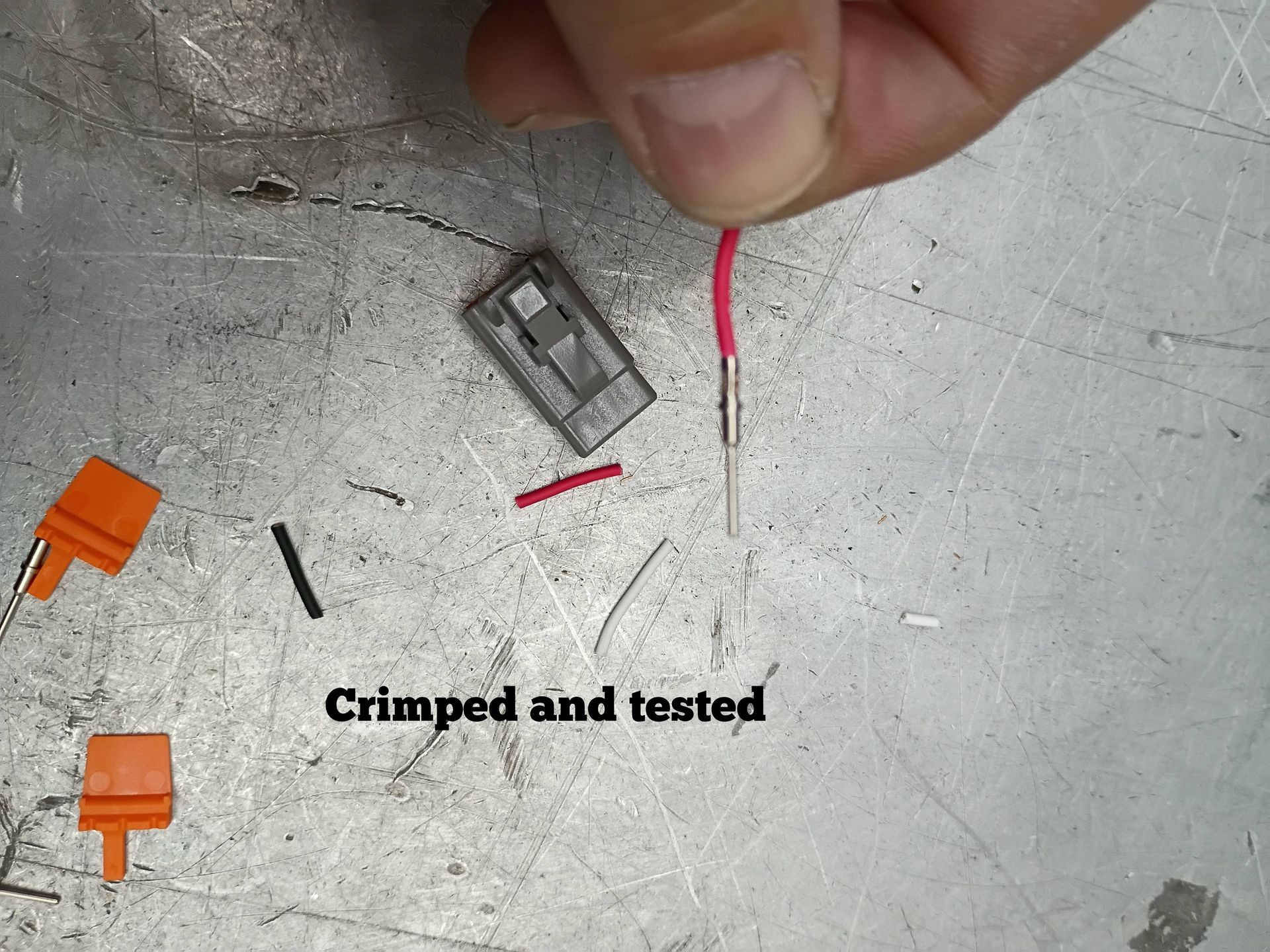 Hand holding a crimped wire near small connectors and text reading “Crimped and tested”