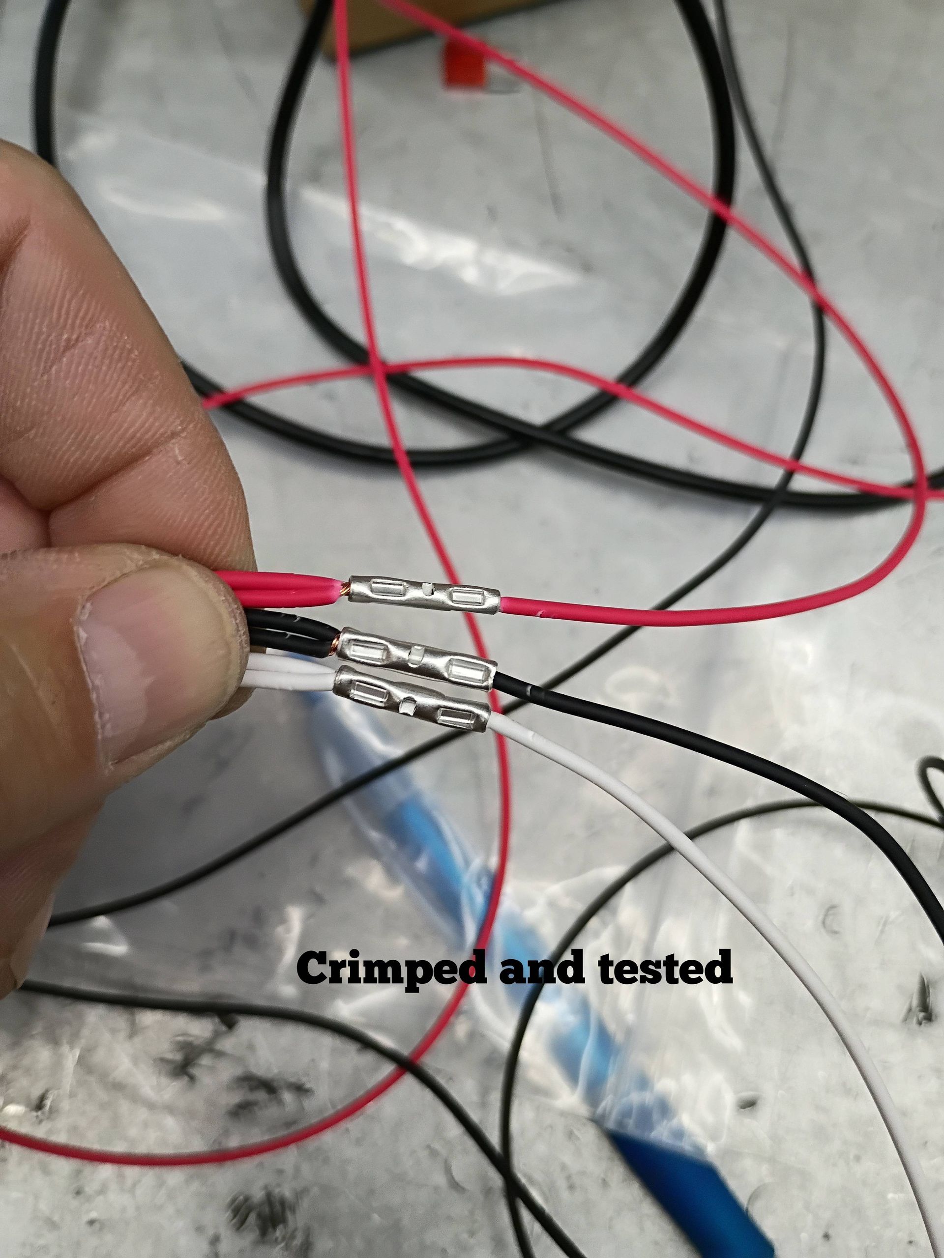 Close-up of crimped red, black, and white wires held in hand, with “Crimped and tested” text visible.