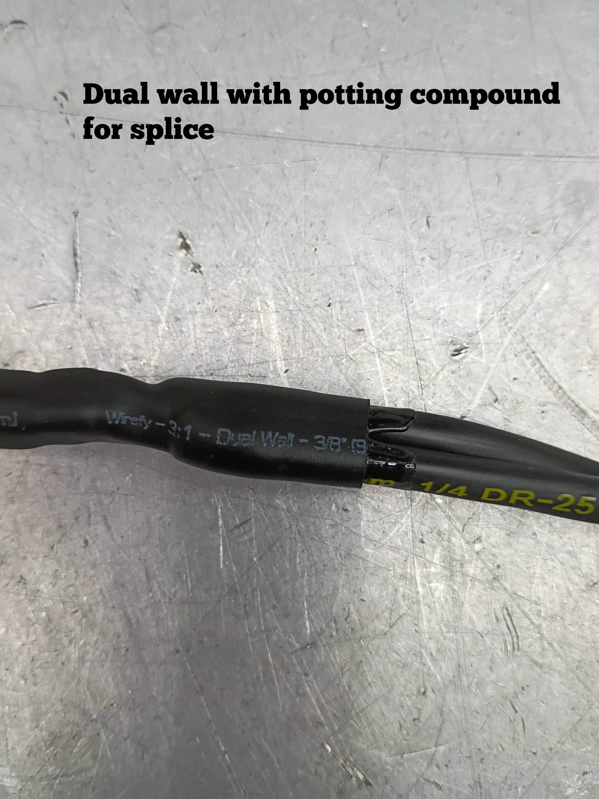 Black dual-wall heat-shrink tubing with potting compound splice on a gray surface