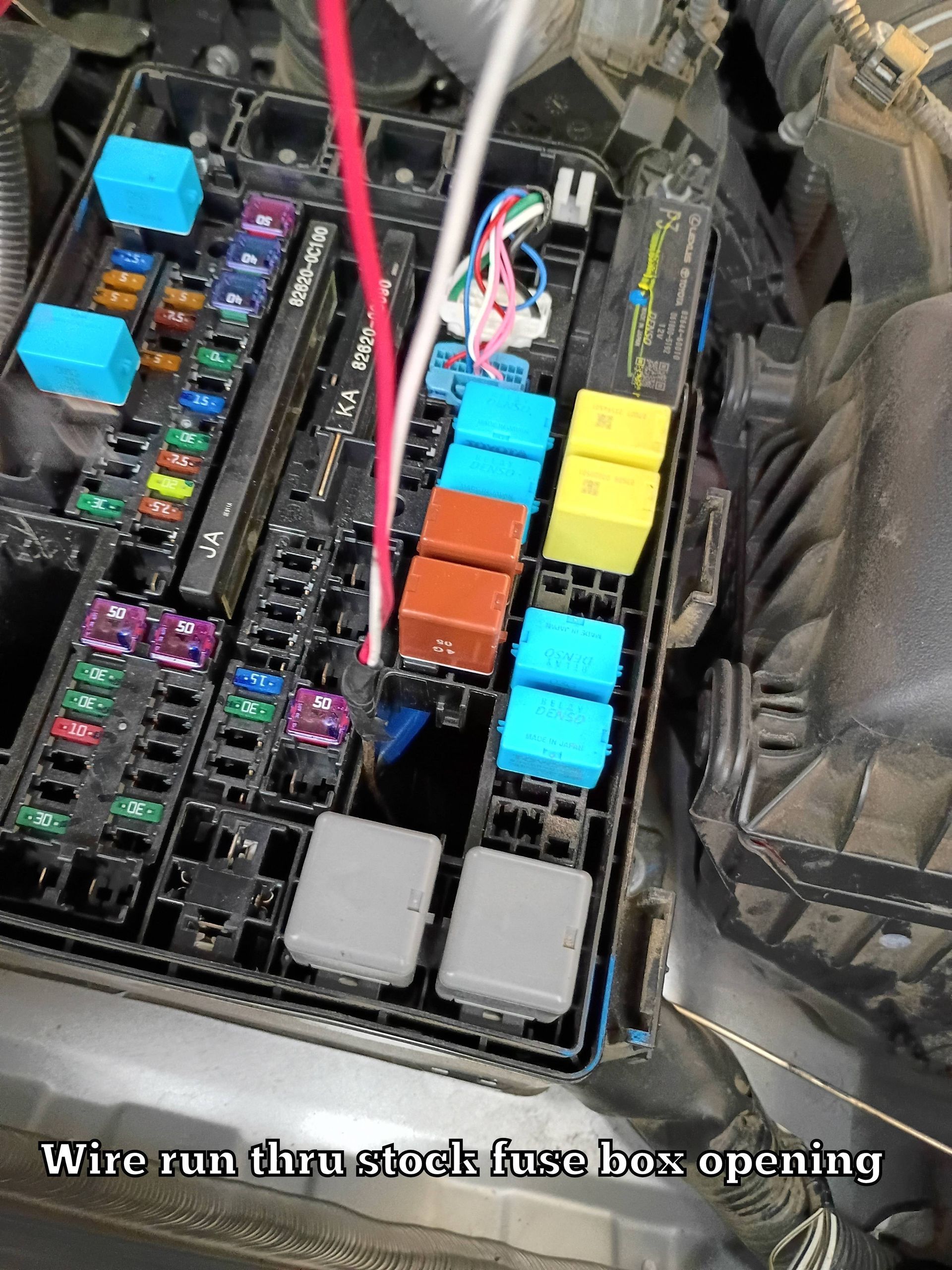 Close-up of a car fuse box with colorful fuses and exposed wiring.