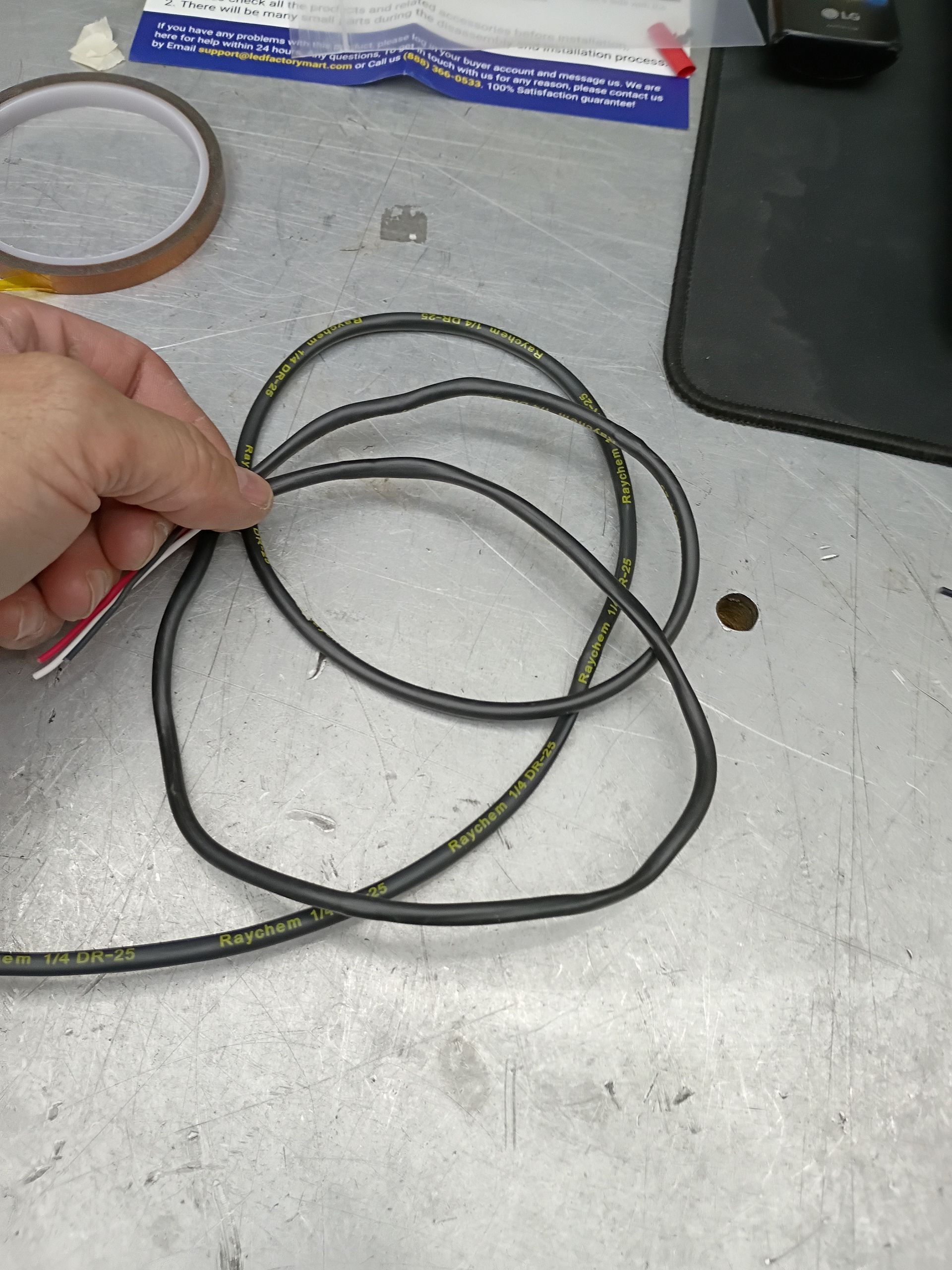 Hand holding a coiled black cable on a gray workbench with a roll of tape nearby