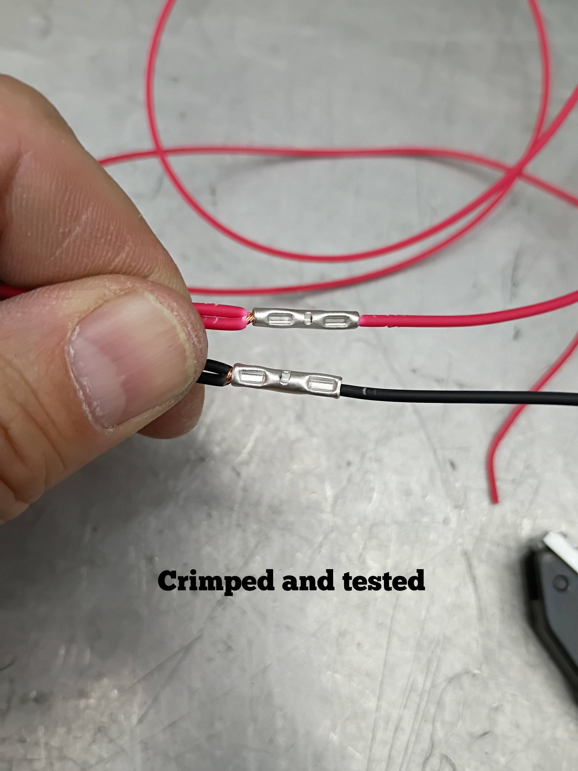 Close-up of crimped red and black wires held together, labeled “Crimped and tested” on a workbench.