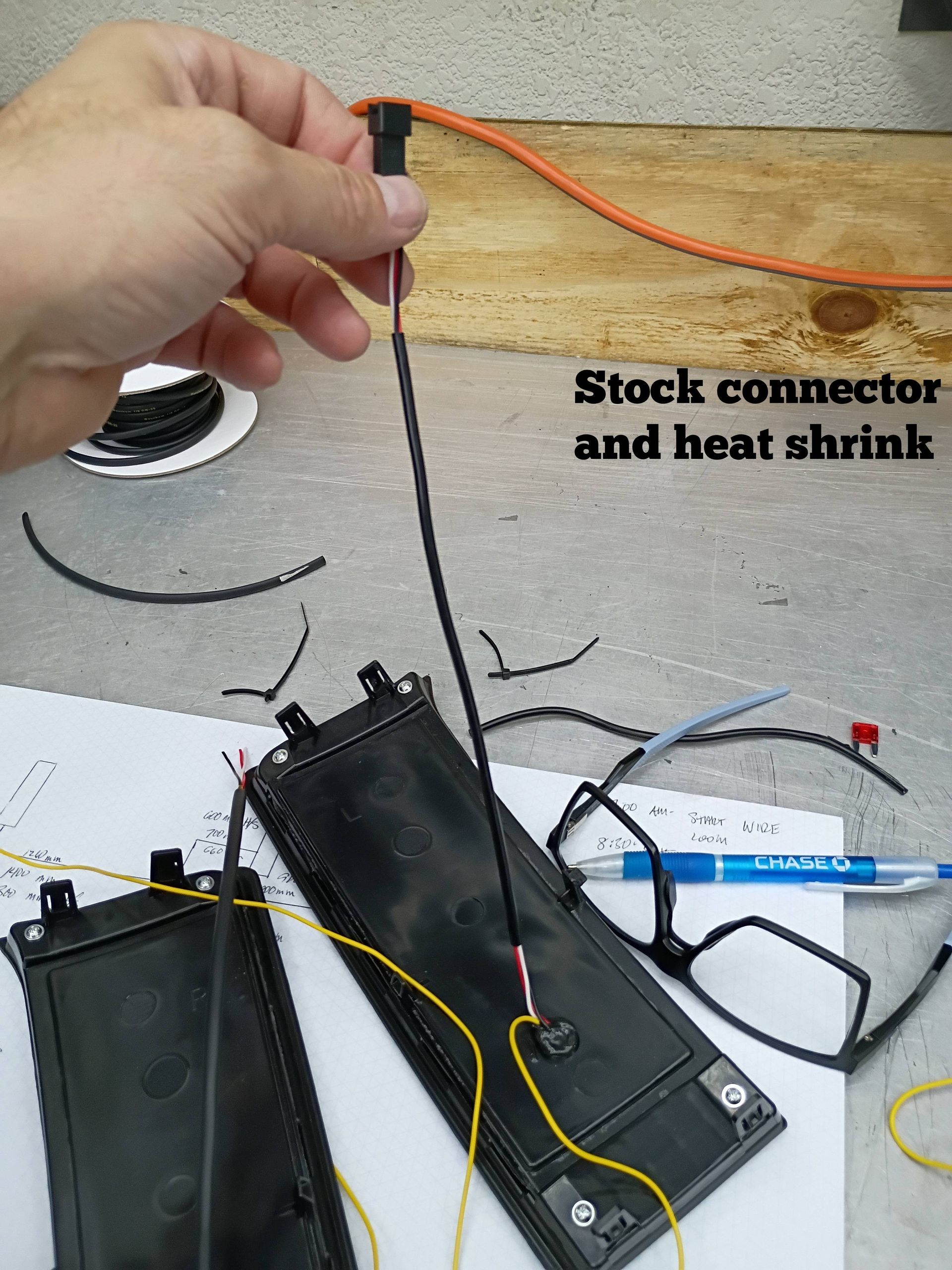 Hand holding orange wire above black battery packs and stock connector with heat shrink labels