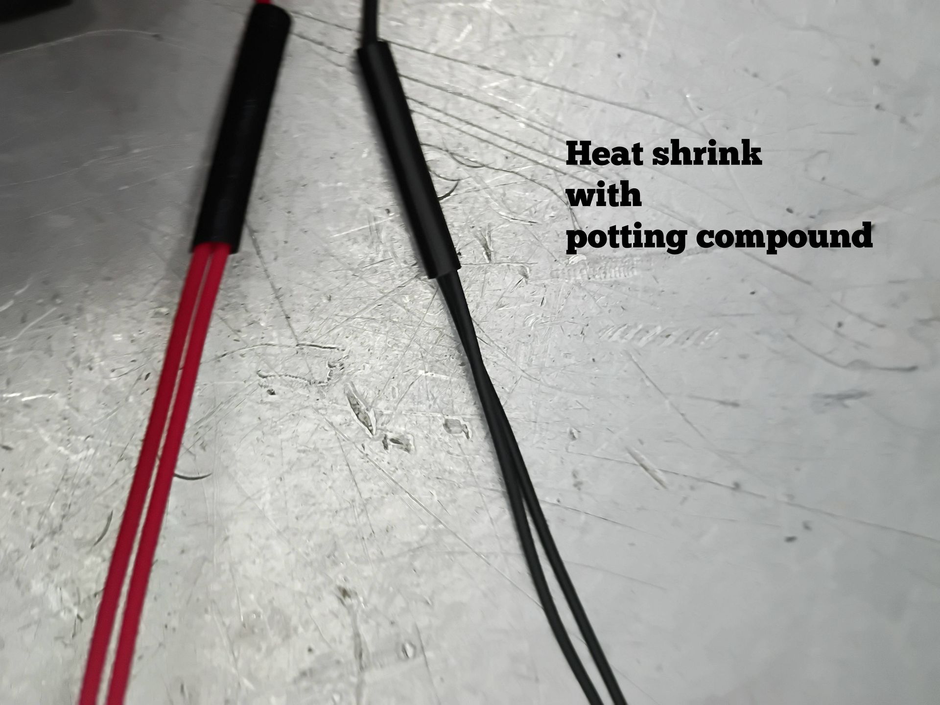 Two wires with black heat-shrink and potting compound on a metal surface