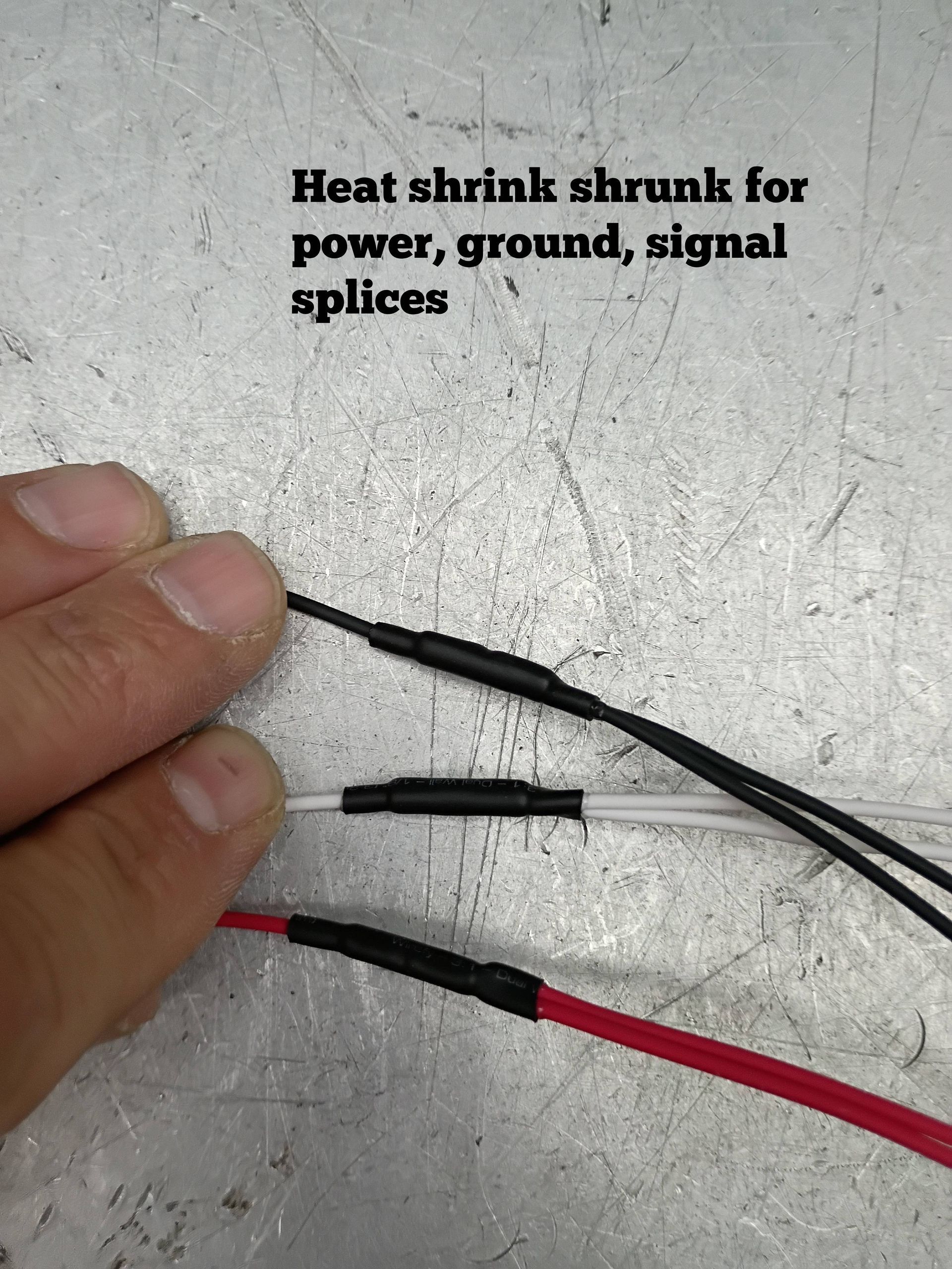Heat-shrink tubing on power, ground, and signal wire splices, with a hand holding the wires.