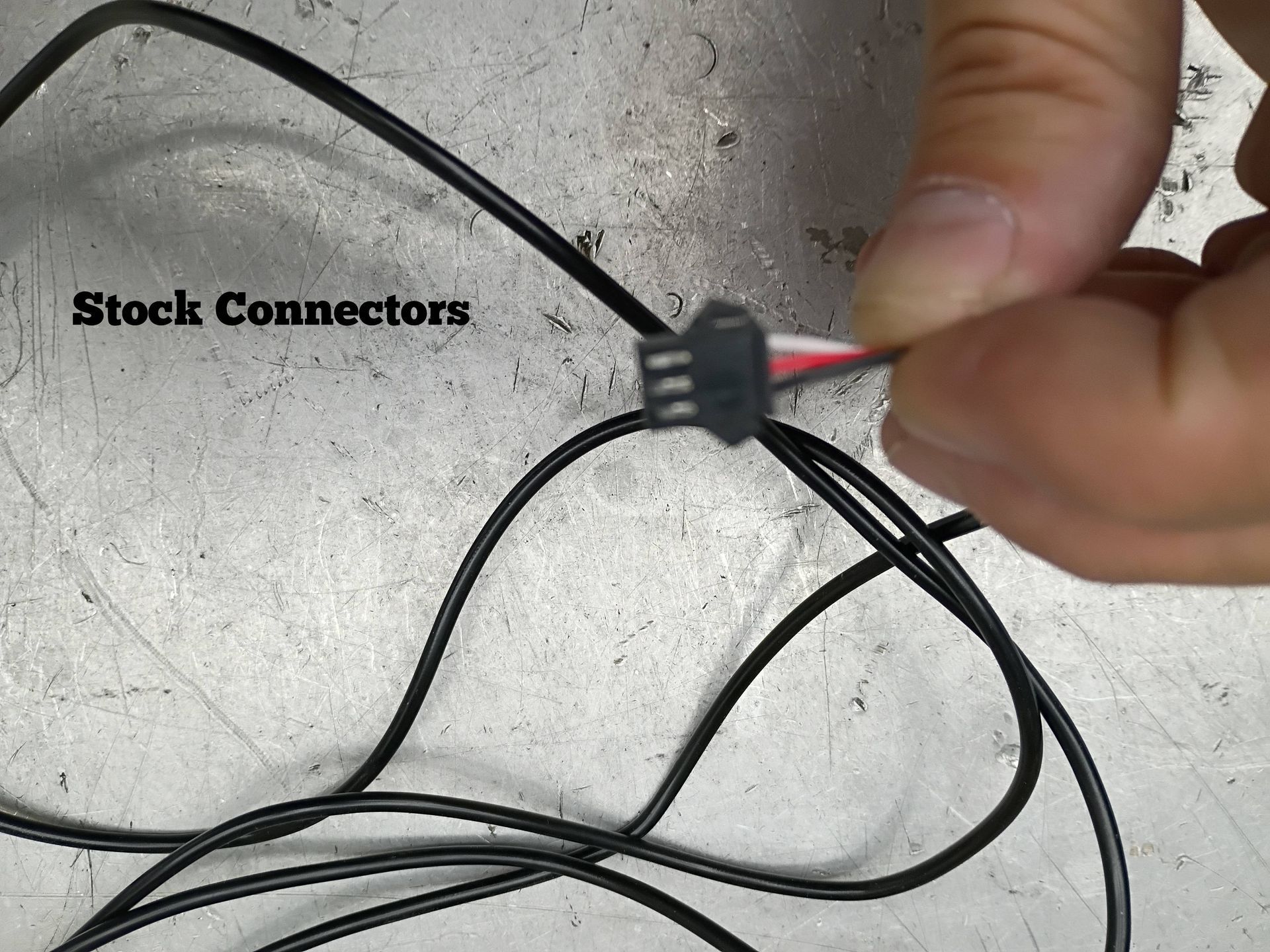 Close-up of a hand holding a black wire connector with red and black wires on a concrete floor.