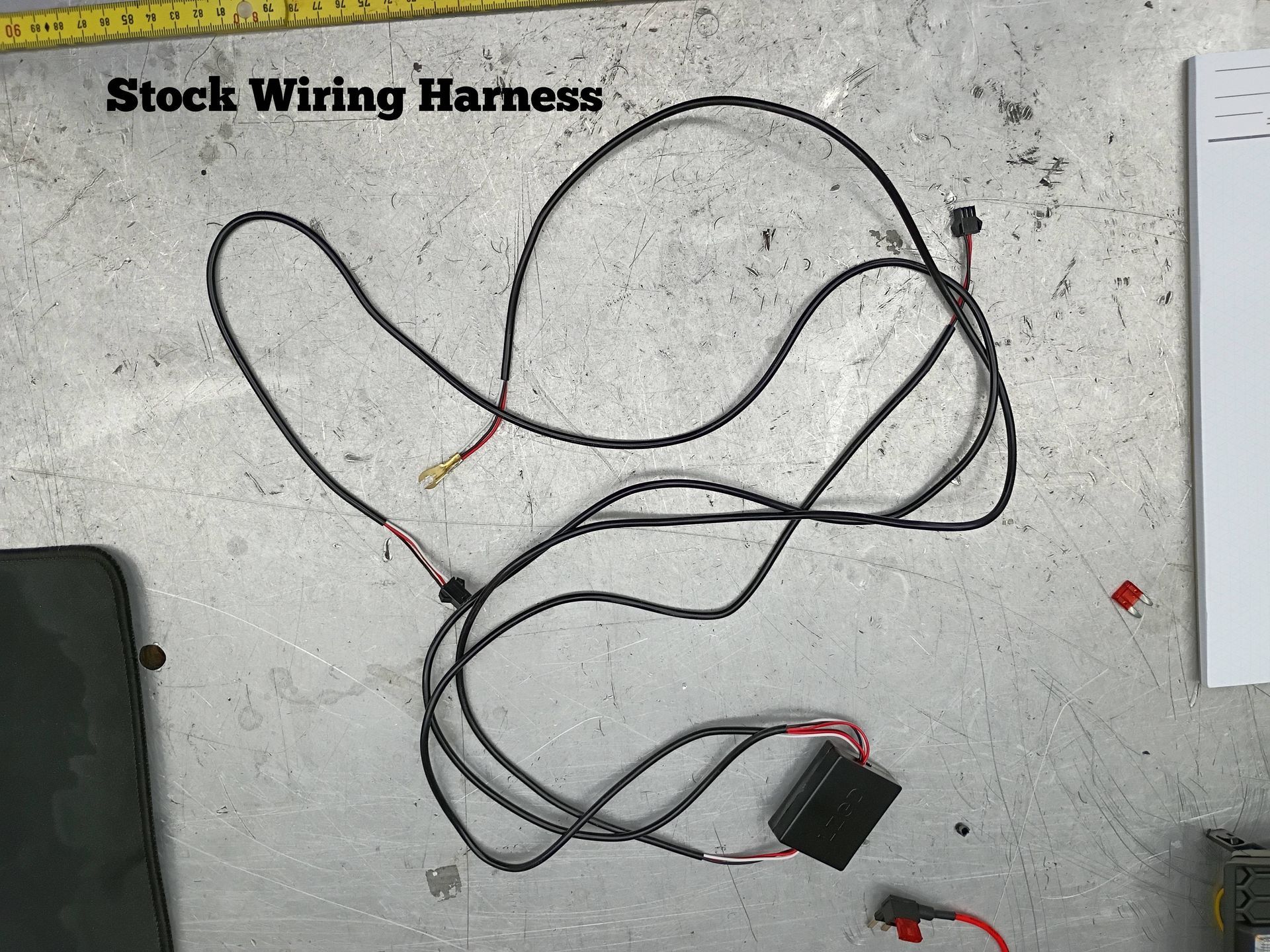 Black wiring harness with connectors and red leads laid on a concrete floor.