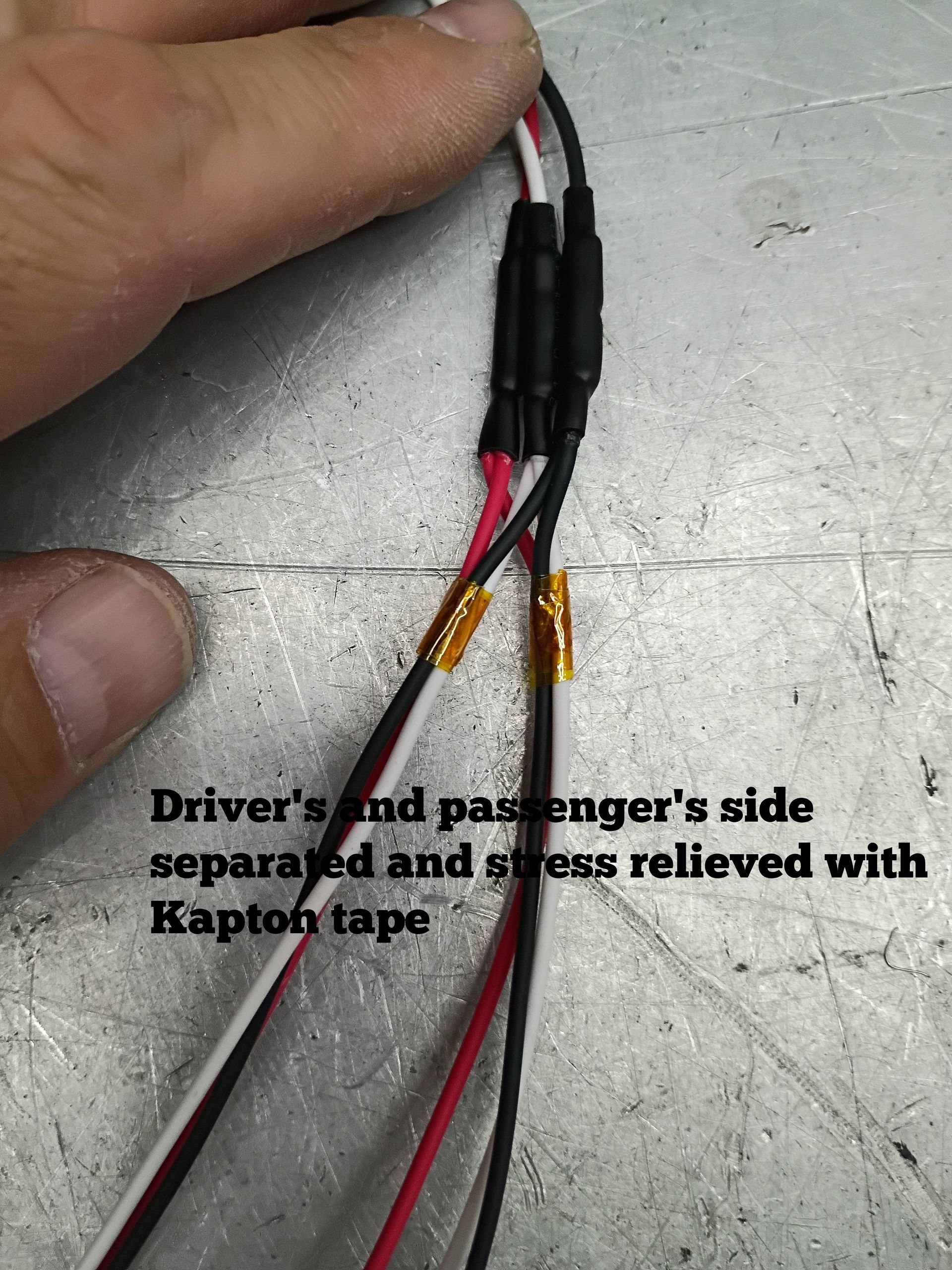 Hand holding black and red wires joined with heat shrink and yellow Kapton tape on a white surface