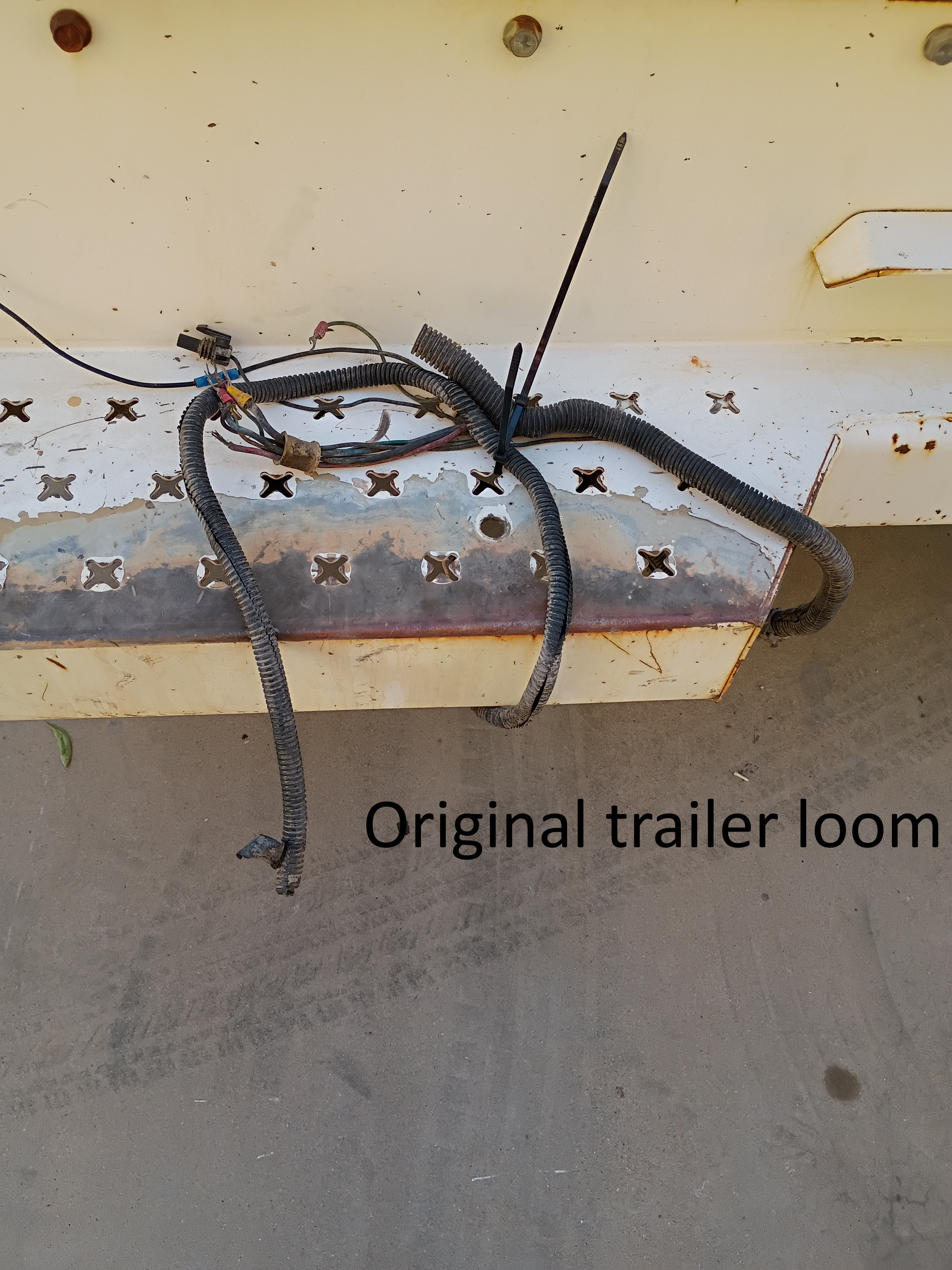 Tangled black trailer wiring loom hanging under a white trailer panel with rust spots