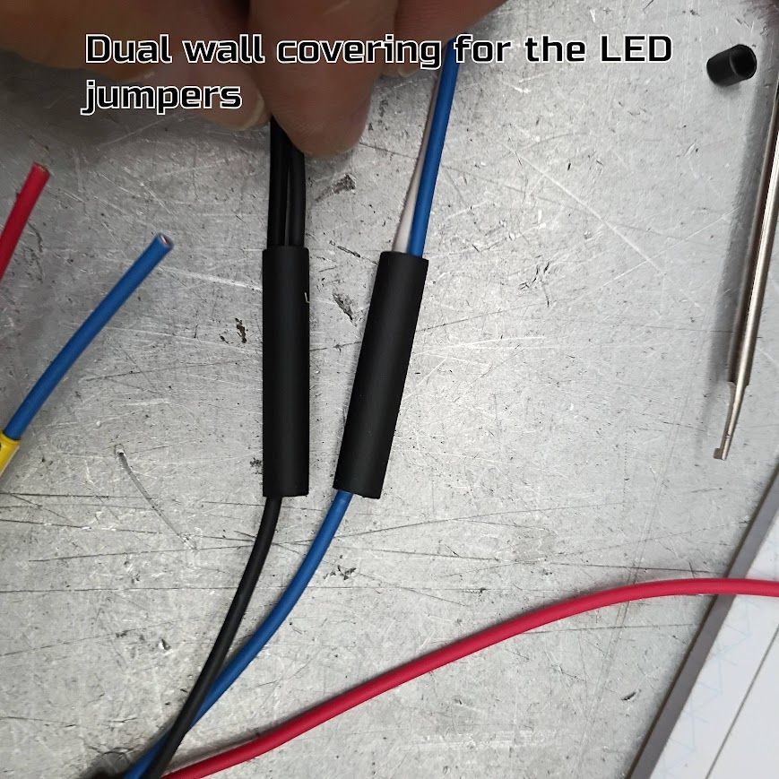 Dual-wall heat-shrink covering black and blue LED jumper wires on a workbench.