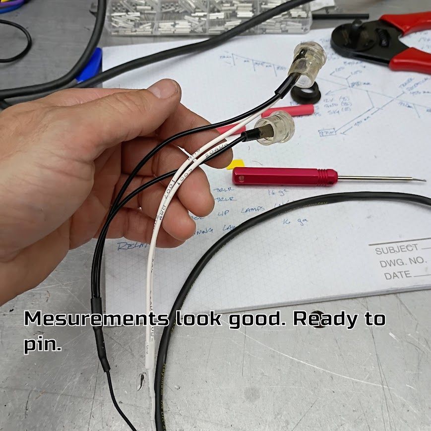 Hand holding wired connectors over a workbench with tools and notes.