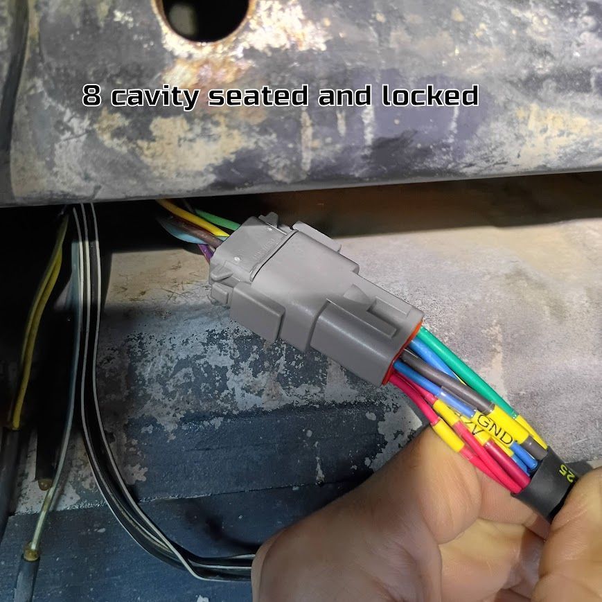 Hand holding a gray 8-cavity connector with multicolored wires in a vehicle wiring area
