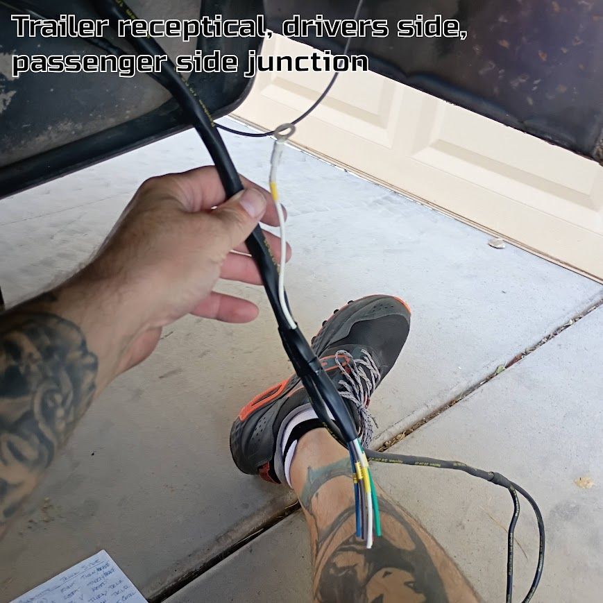 Hand holding a trailer receptacle wiring harness with exposed colored wires over a garage floor.