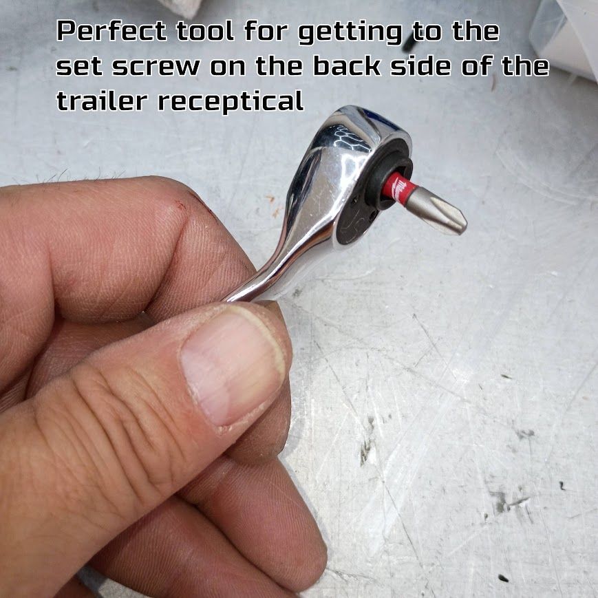 Hand holding a small chrome ratchet tool with a red socket adapter on a workbench.