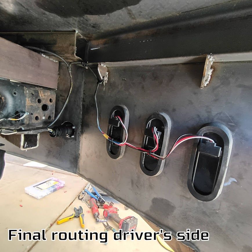 Car wiring harness routed through driver-side firewall openings, with tools on a work surface.