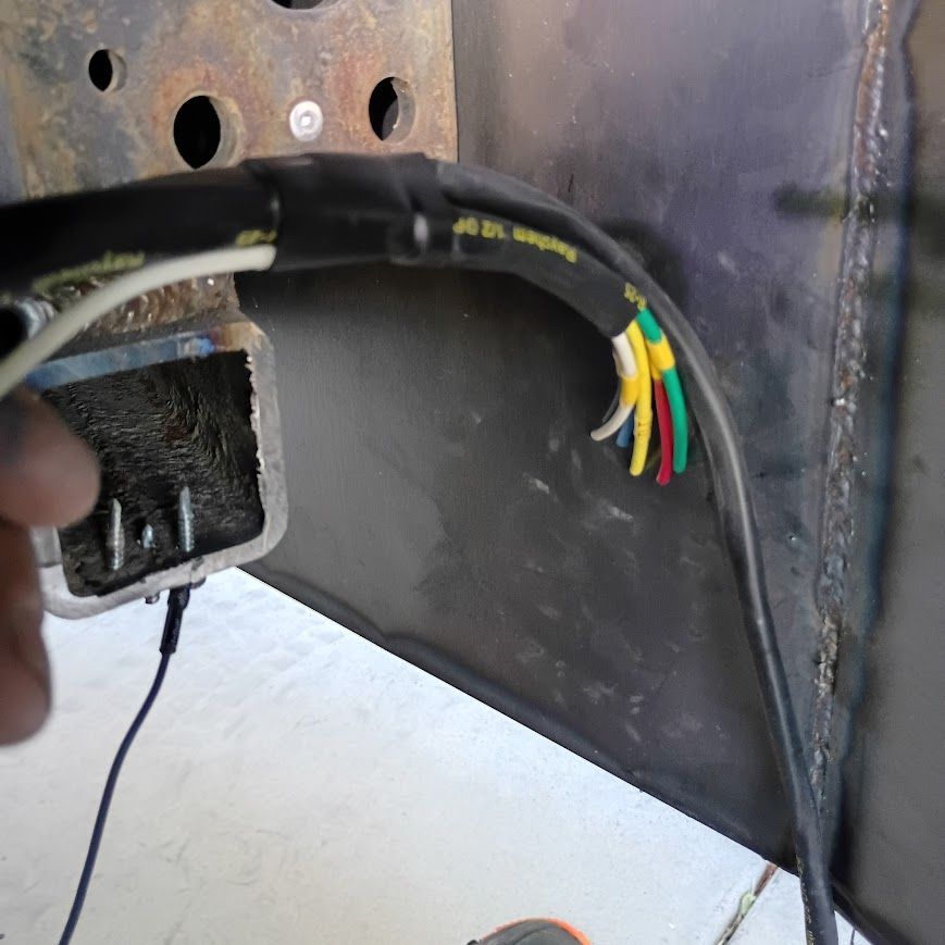 Loose multicolored wires inside a metal electrical box with a black cable running across it