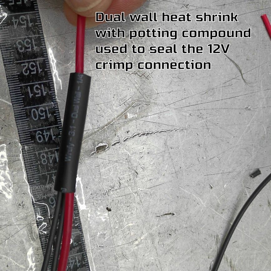 Close-up of red and black wires joined by a black heat-shrink sleeve on a workbench, with text label visible.