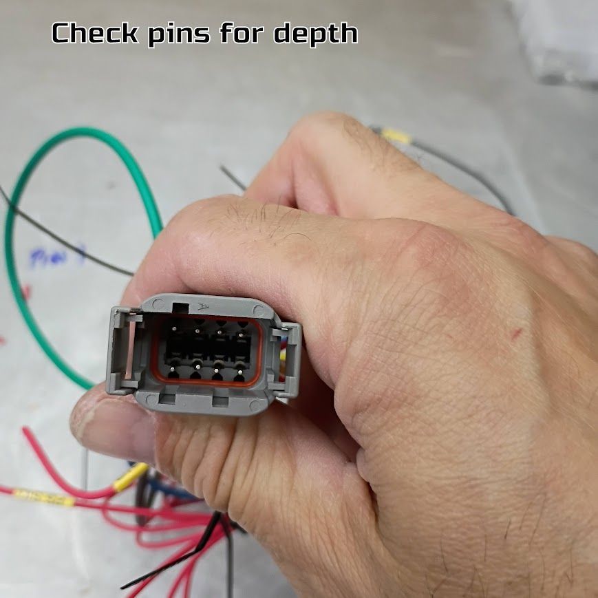 Close-up of a hand holding a gray electrical connector with colored wires on a workbench.