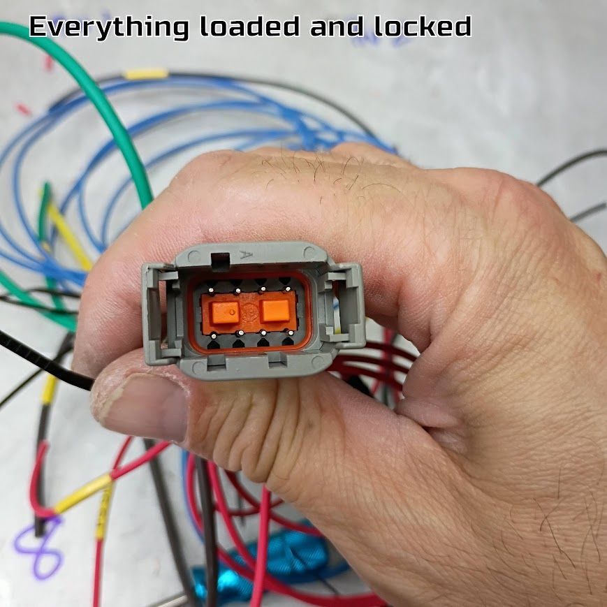 Hand holding a gray electrical connector with orange pins and colorful wires in the background